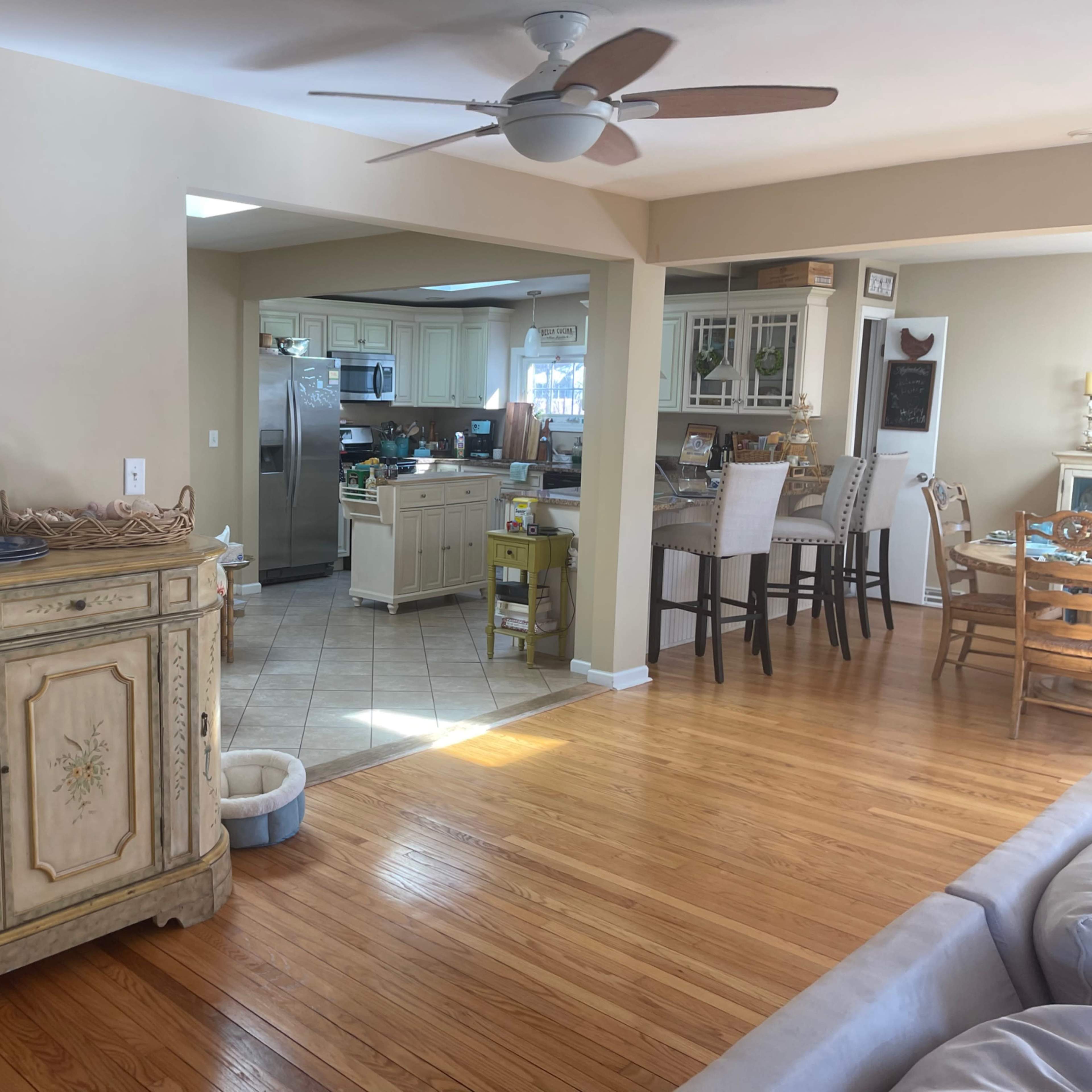 A spacious living area with a wooden floor, a decorative cabinet, and an open kitchen in the background.