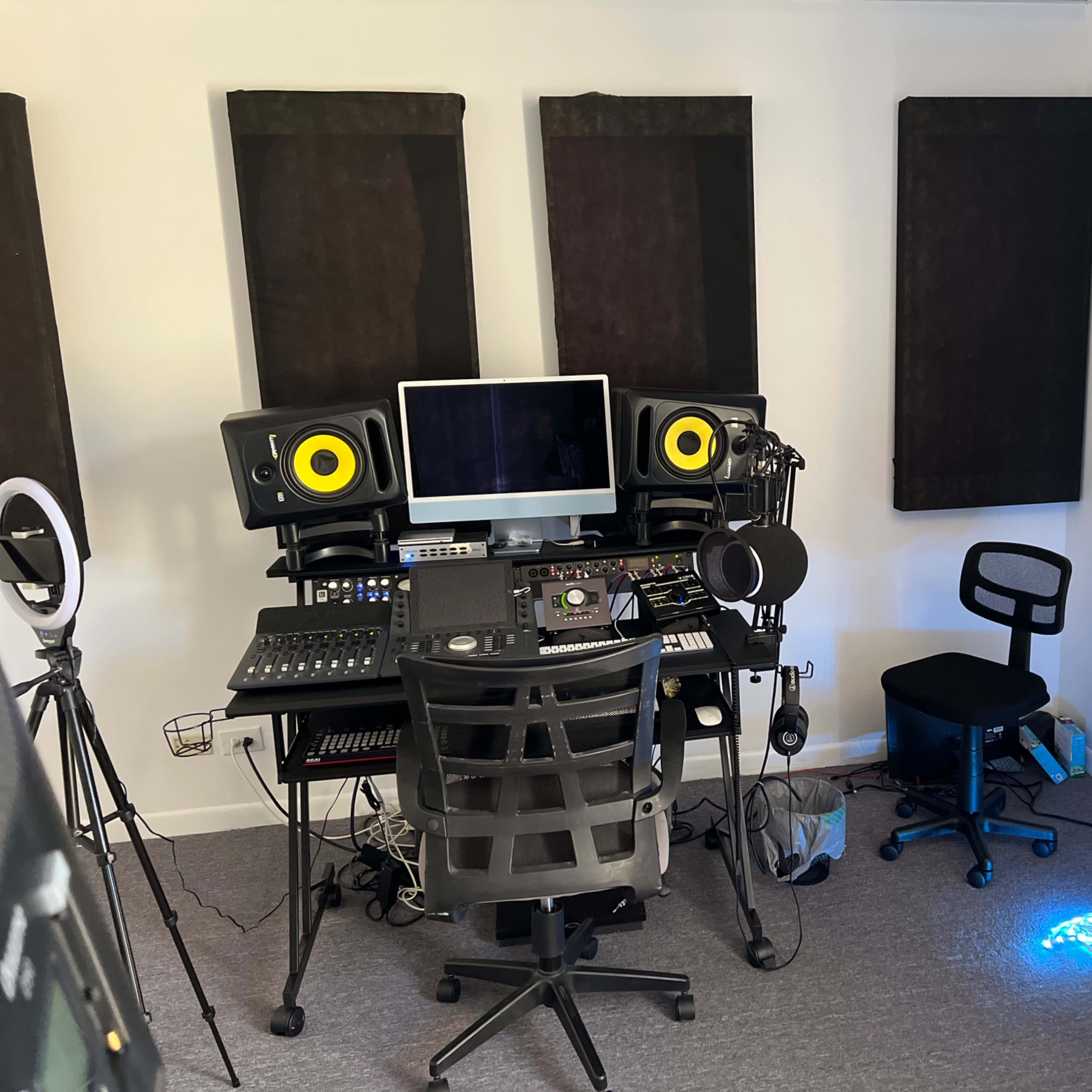 A music studio is equipped with soundproof panels, a computer, audio mixing equipment, and microphones.
