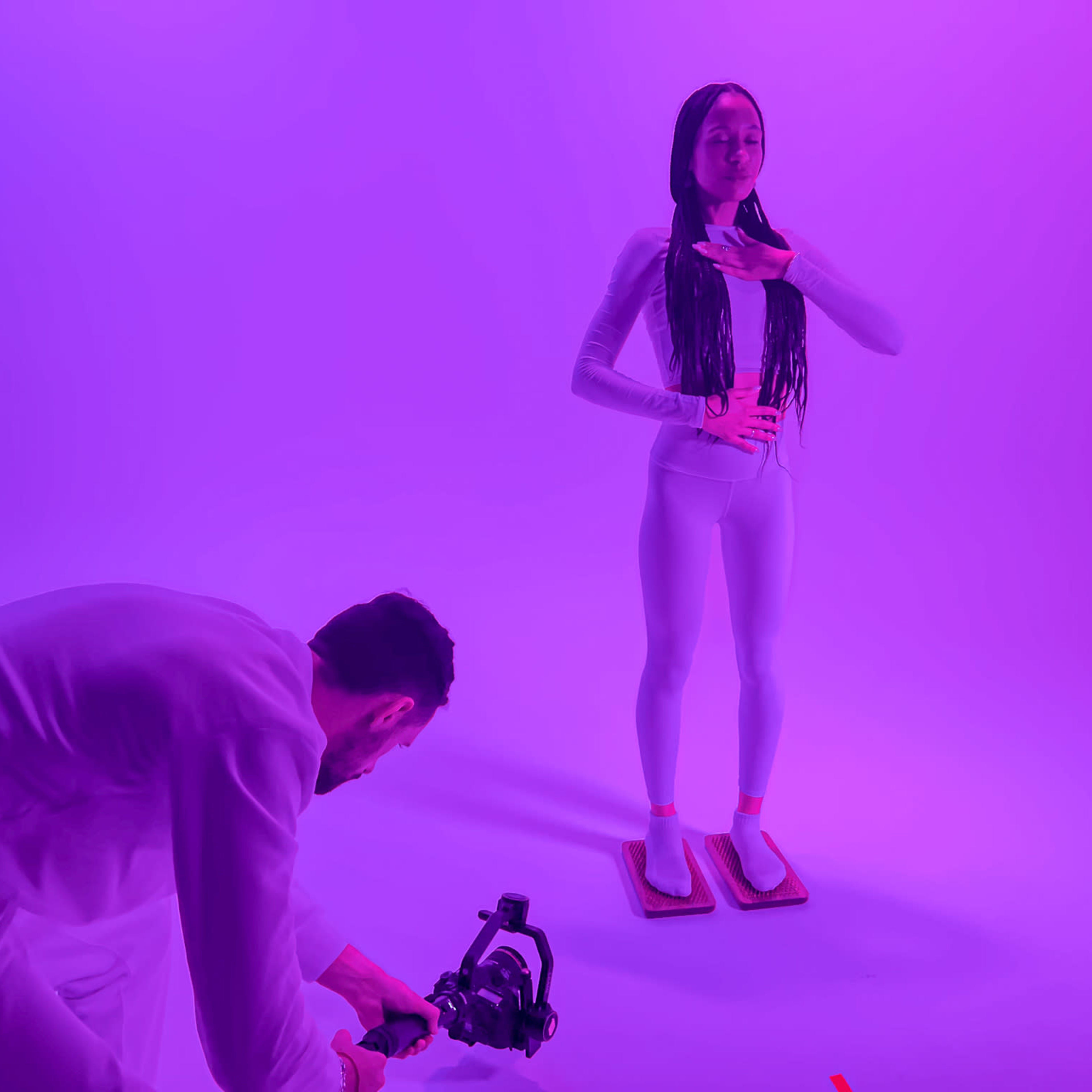 A photographer captures a model in a bright purple studio while she poses on a raised platform.