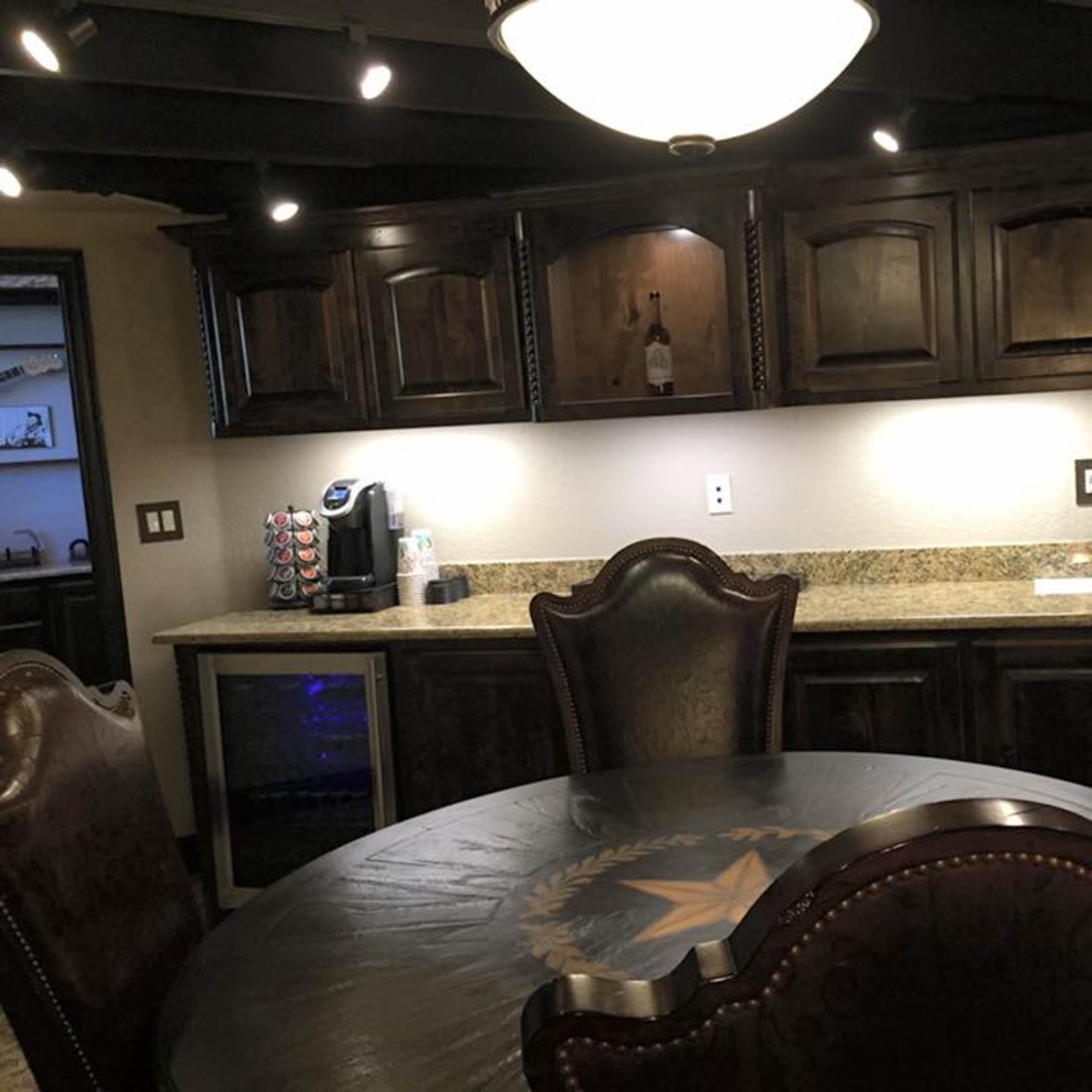 A kitchen area featuring dark wooden cabinetry, a granite countertop, a round table with ornate chairs, and a beverage cooler.