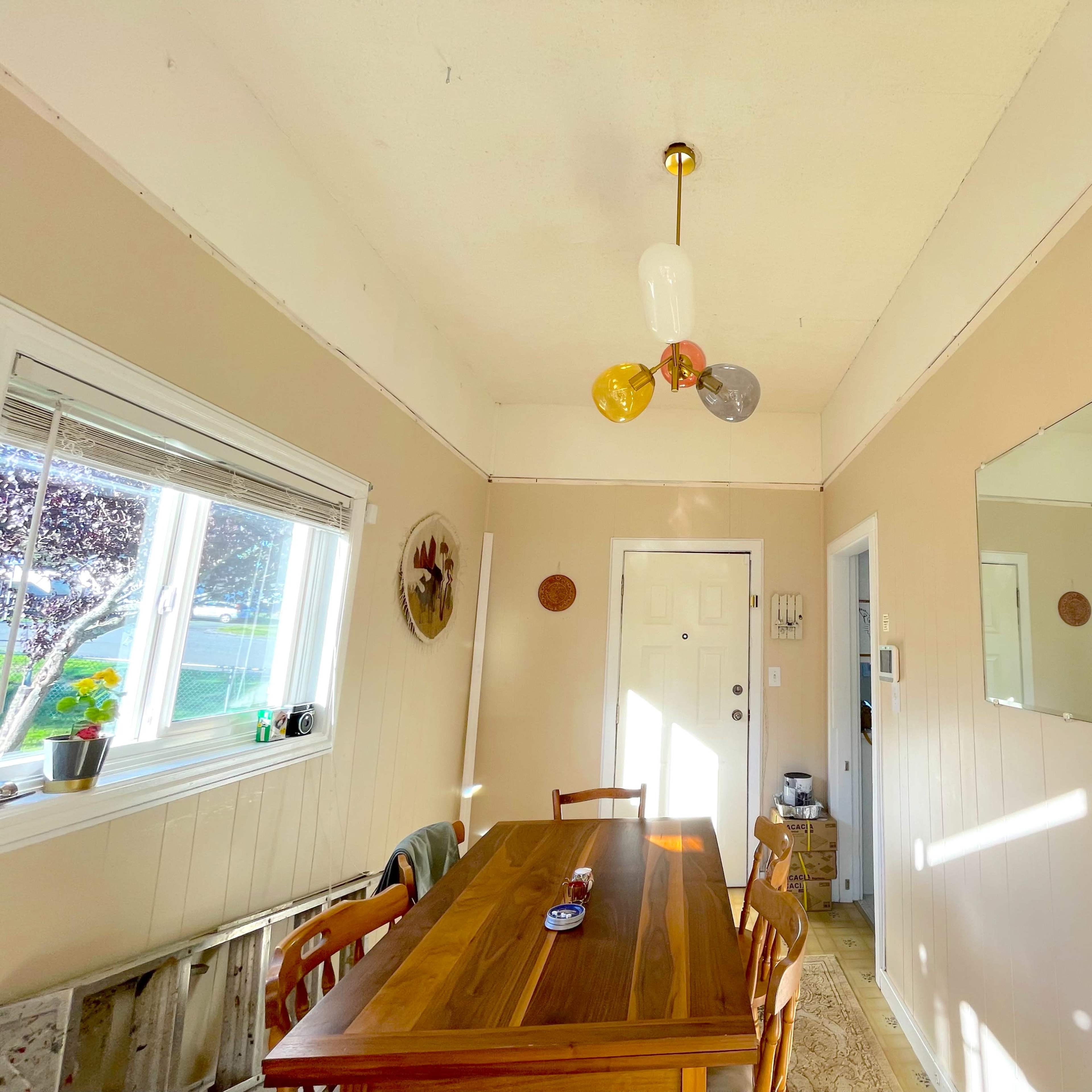 A light-filled dining area with a wooden table, four chairs, and a ceiling light fixture with colorful bulbs.