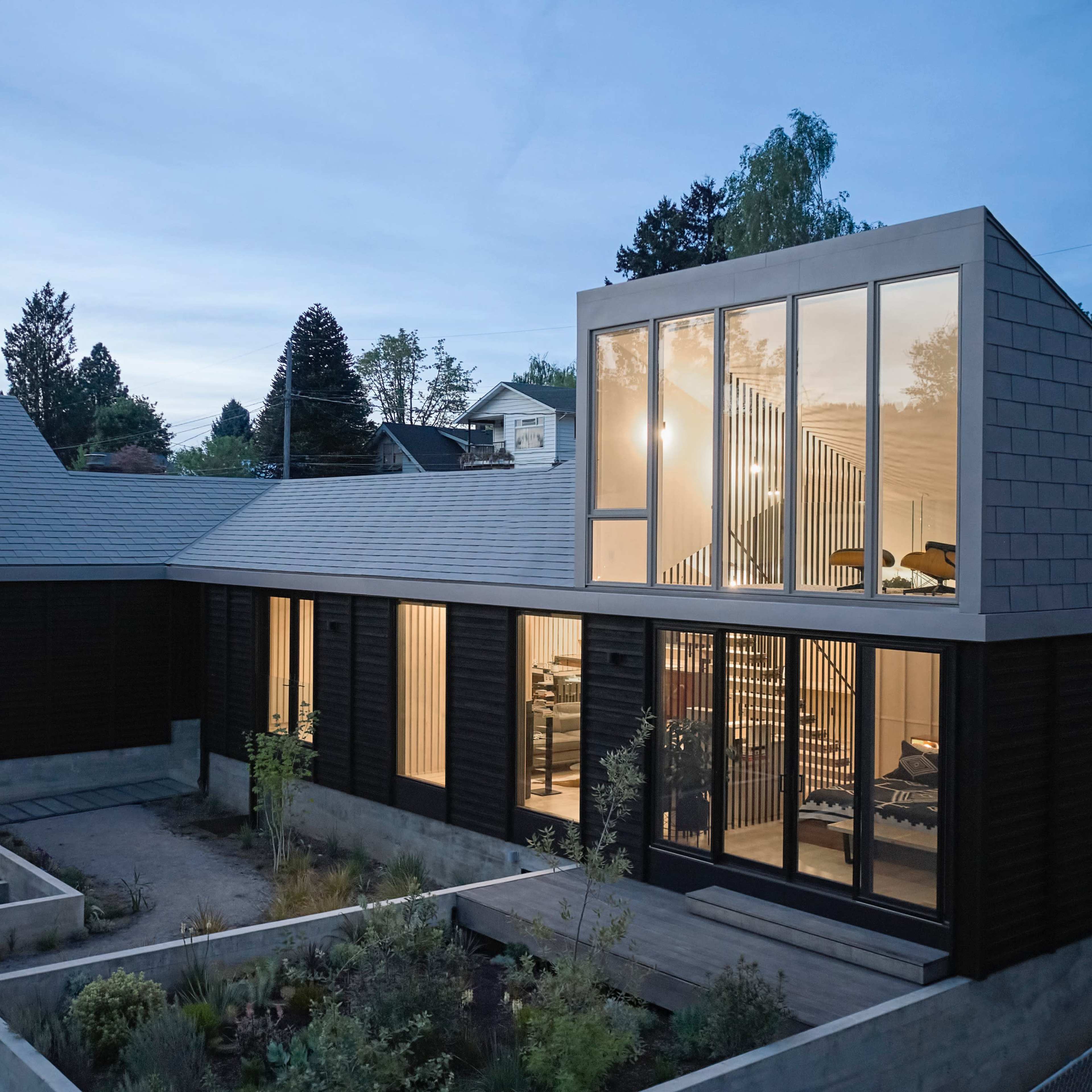 A modern house with large windows and a sloped roof, surrounded by landscaped gardens in the early evening light.