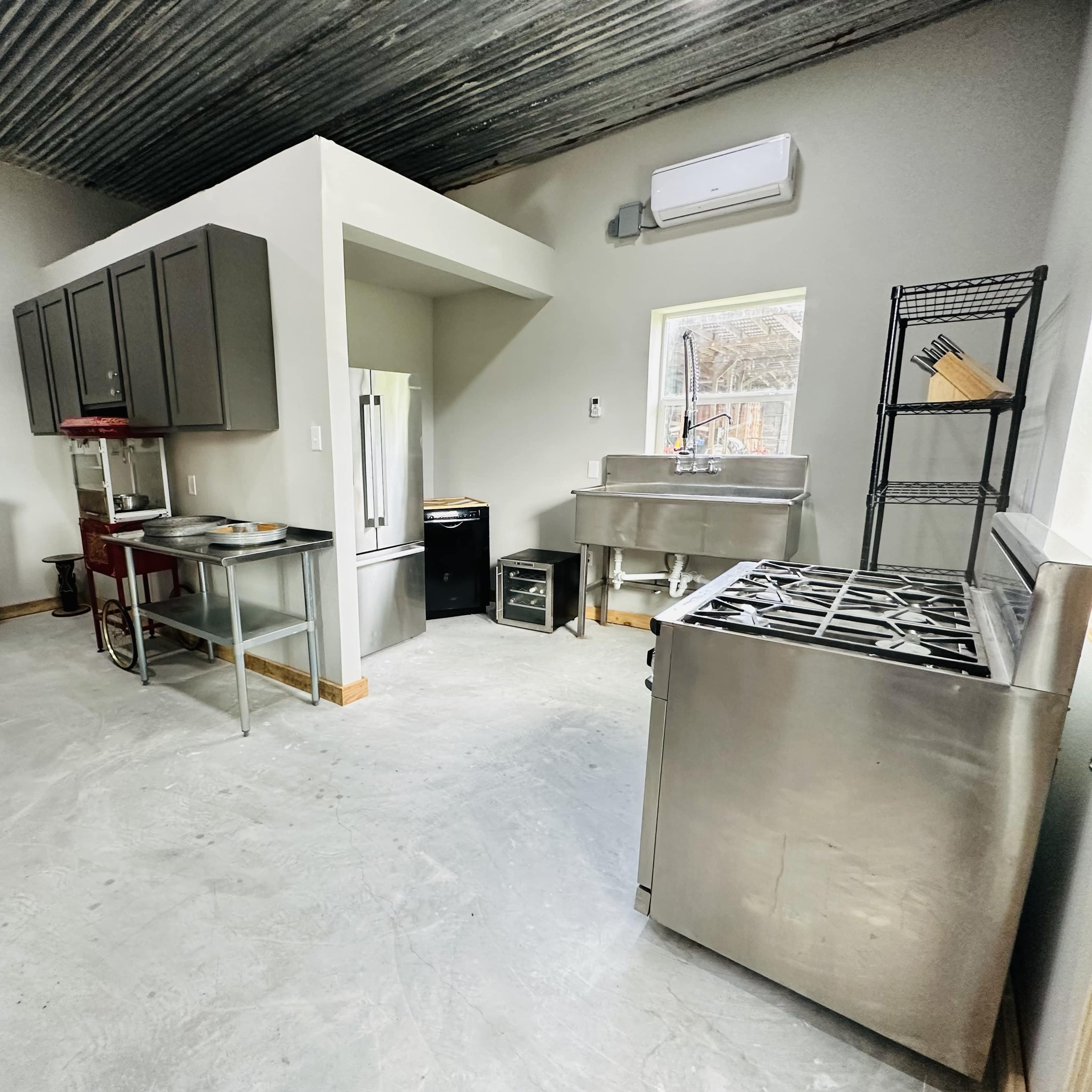 A spacious kitchen with stainless steel appliances, a wooden chest, and a high ceiling with exposed metal beams.