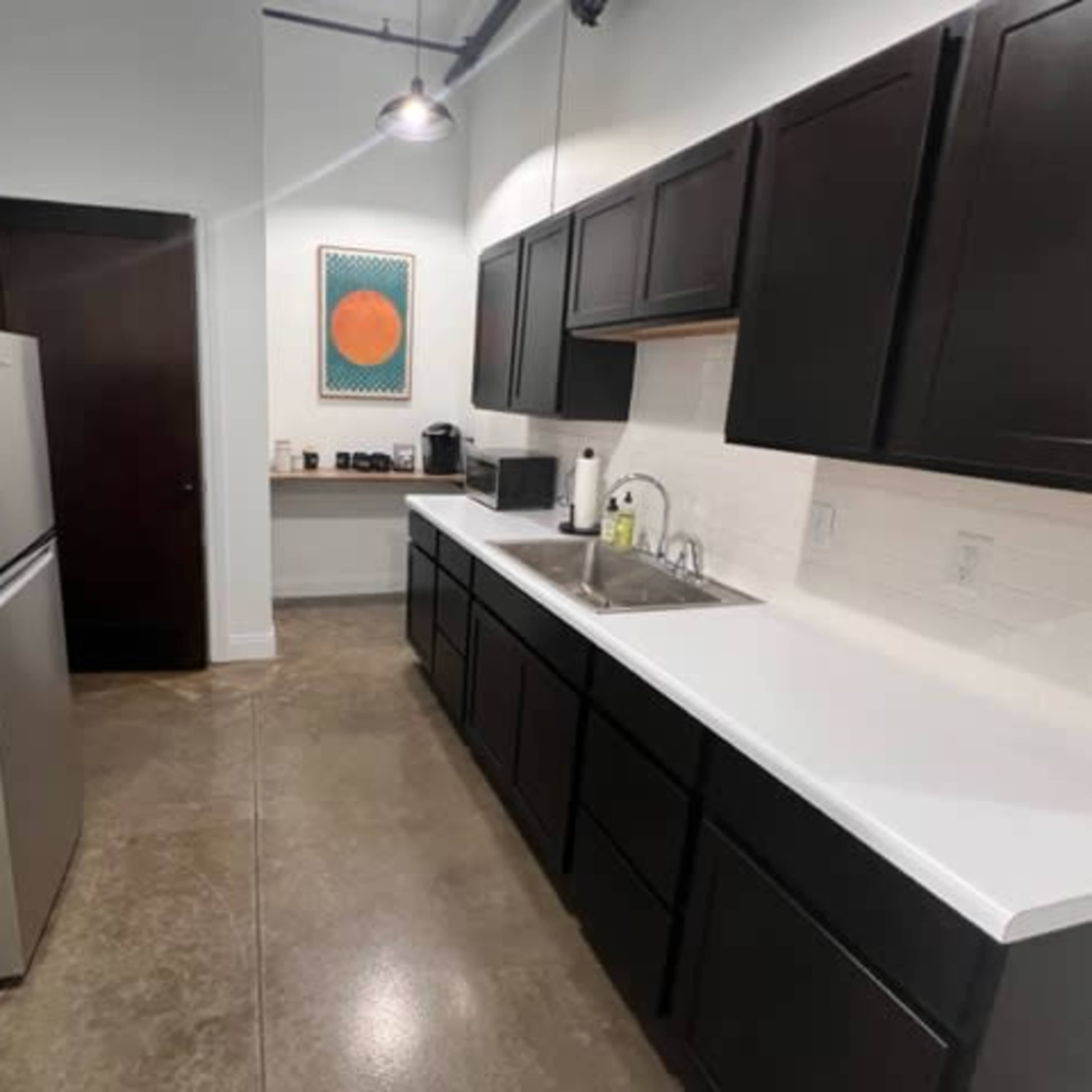 A kitchen featuring dark cabinets, a white countertop, stainless steel appliances, and a simple wall decoration.