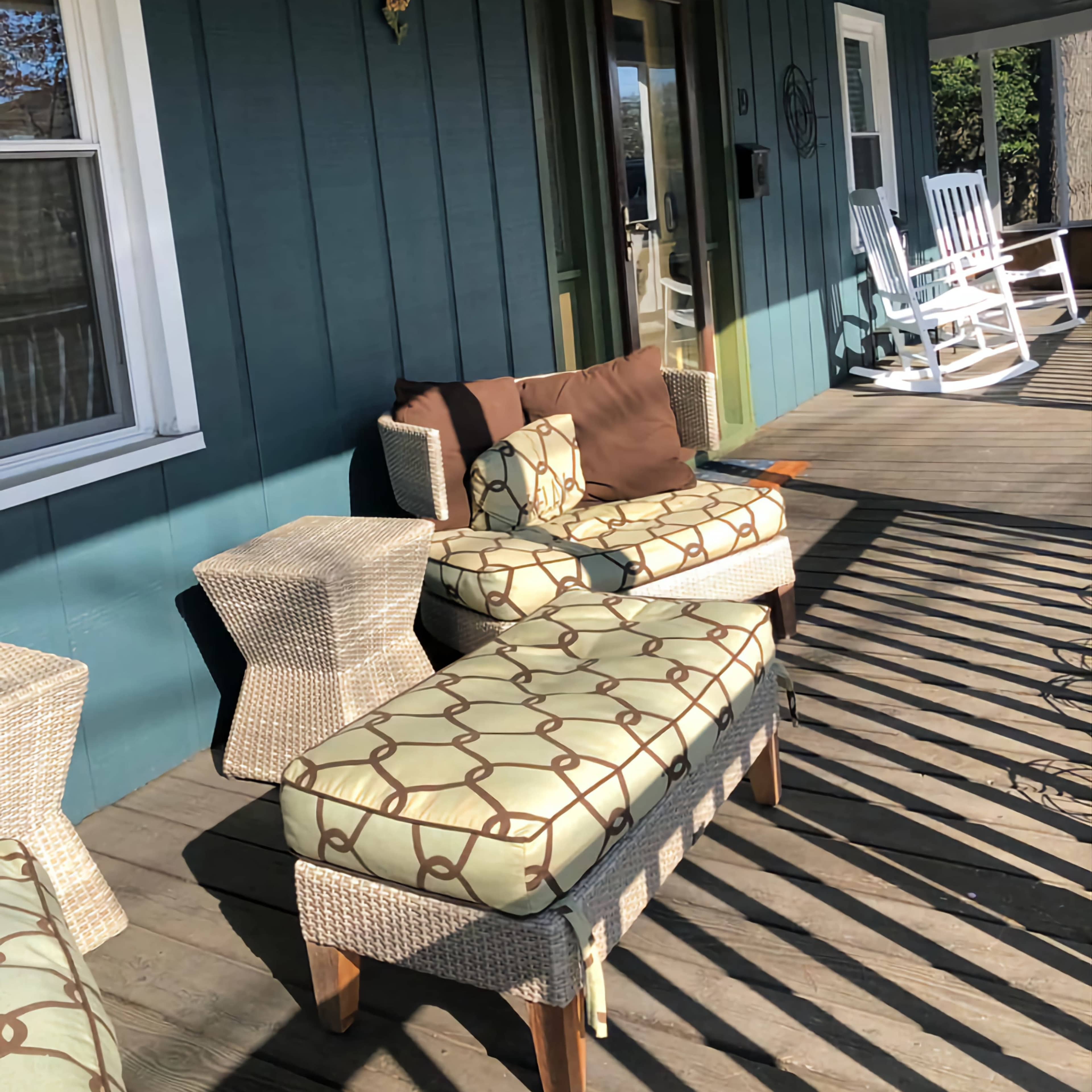 A porch with wicker furniture, including a loveseat and a bench, set against a teal wall and wooden flooring.