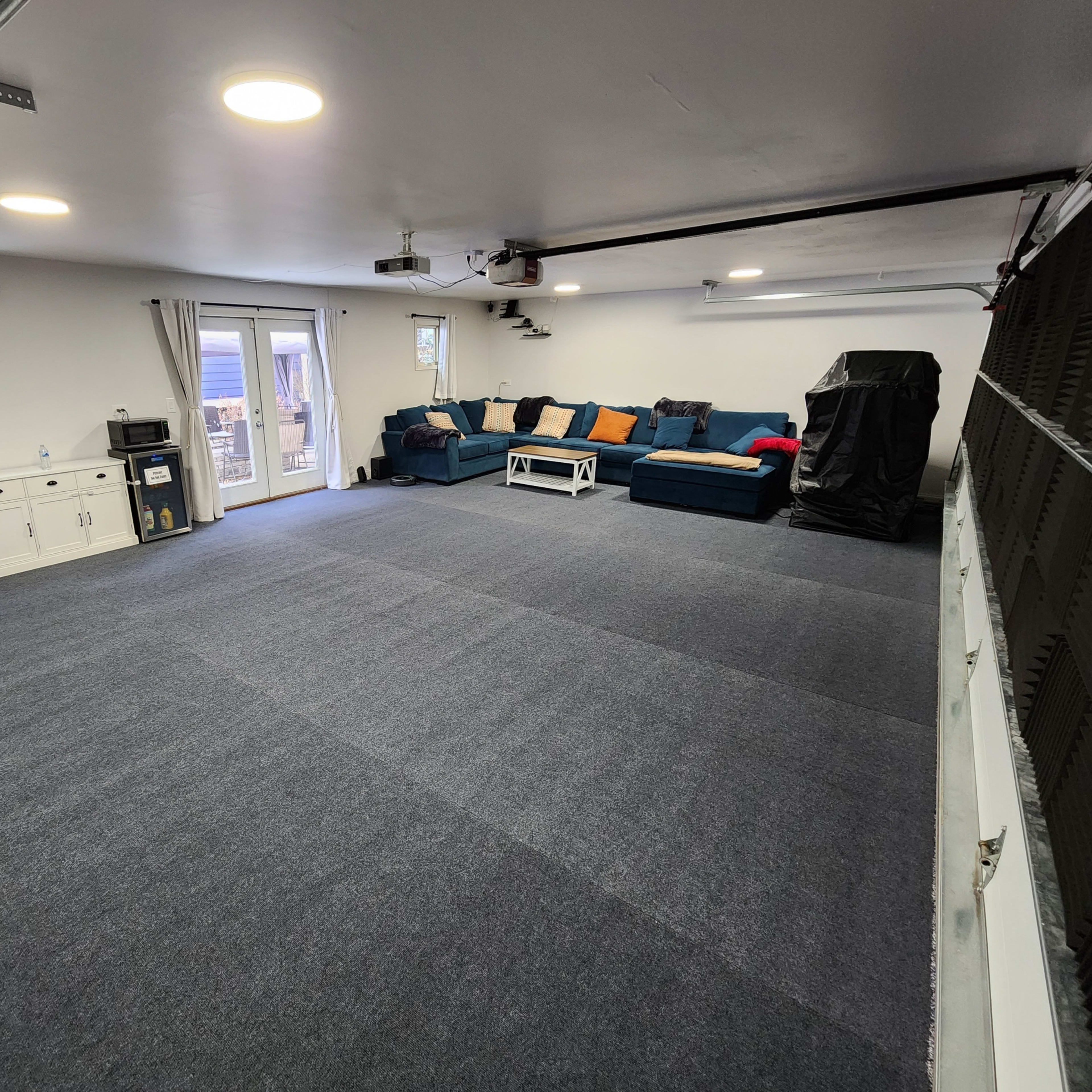 A large, empty room with gray carpet, a blue sectional sofa, a coffee table, and a sliding door leading to an outdoor area.