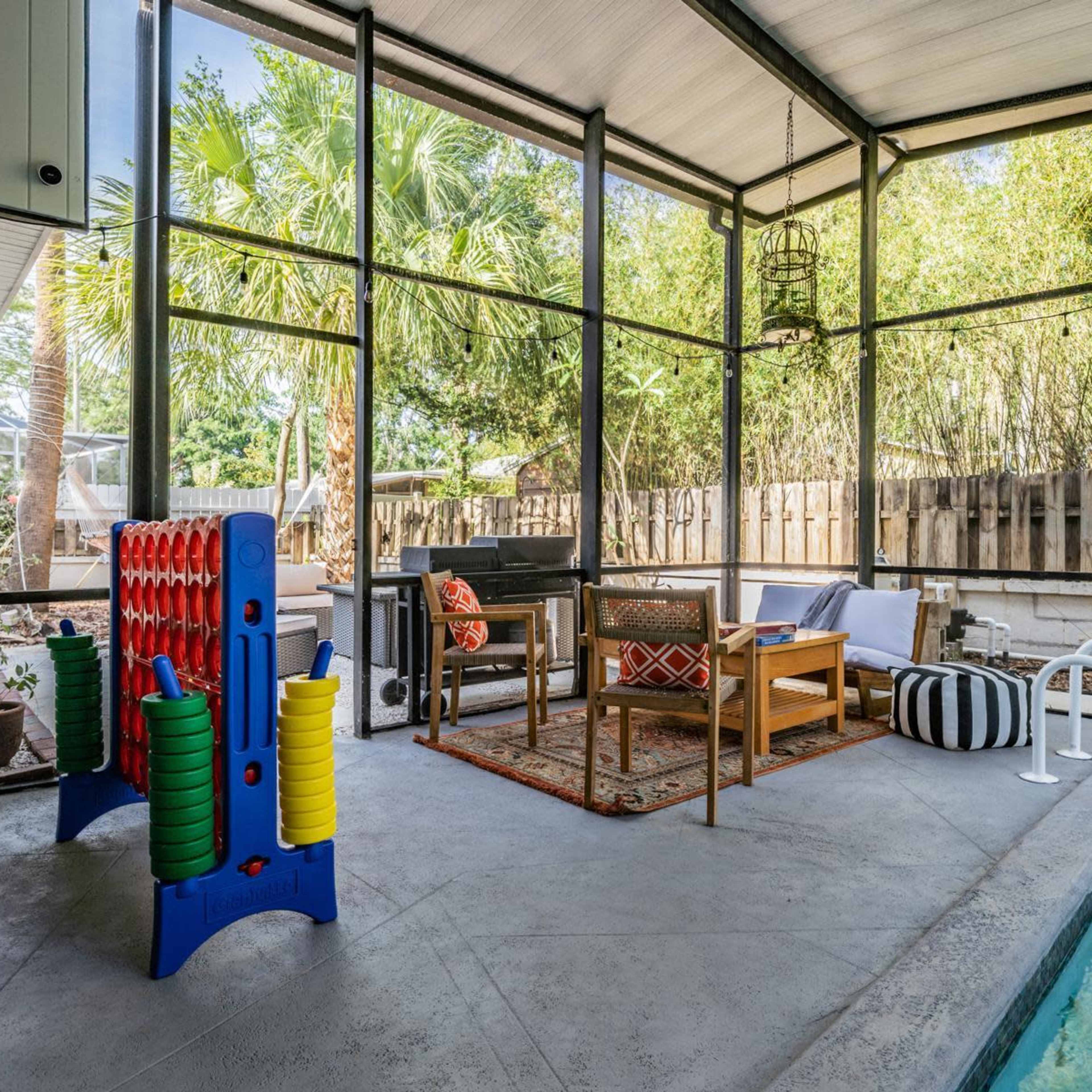 A screened-in patio with a seating area and a swimming pool, featuring games and decorative elements.