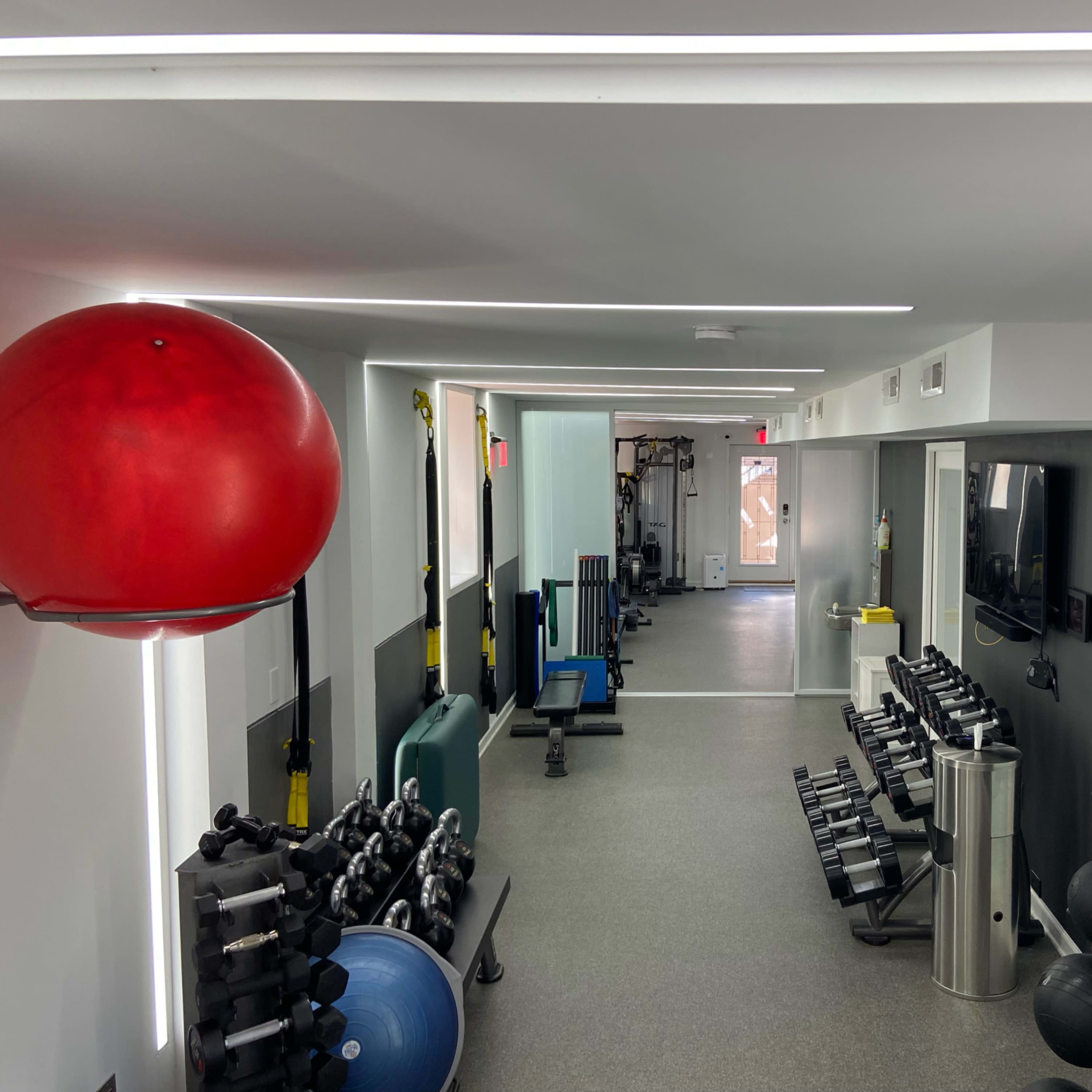 A modern gym layout with various exercise equipment, including weights, exercise balls, and fitness machines, organized neatly in a well-lit space.
