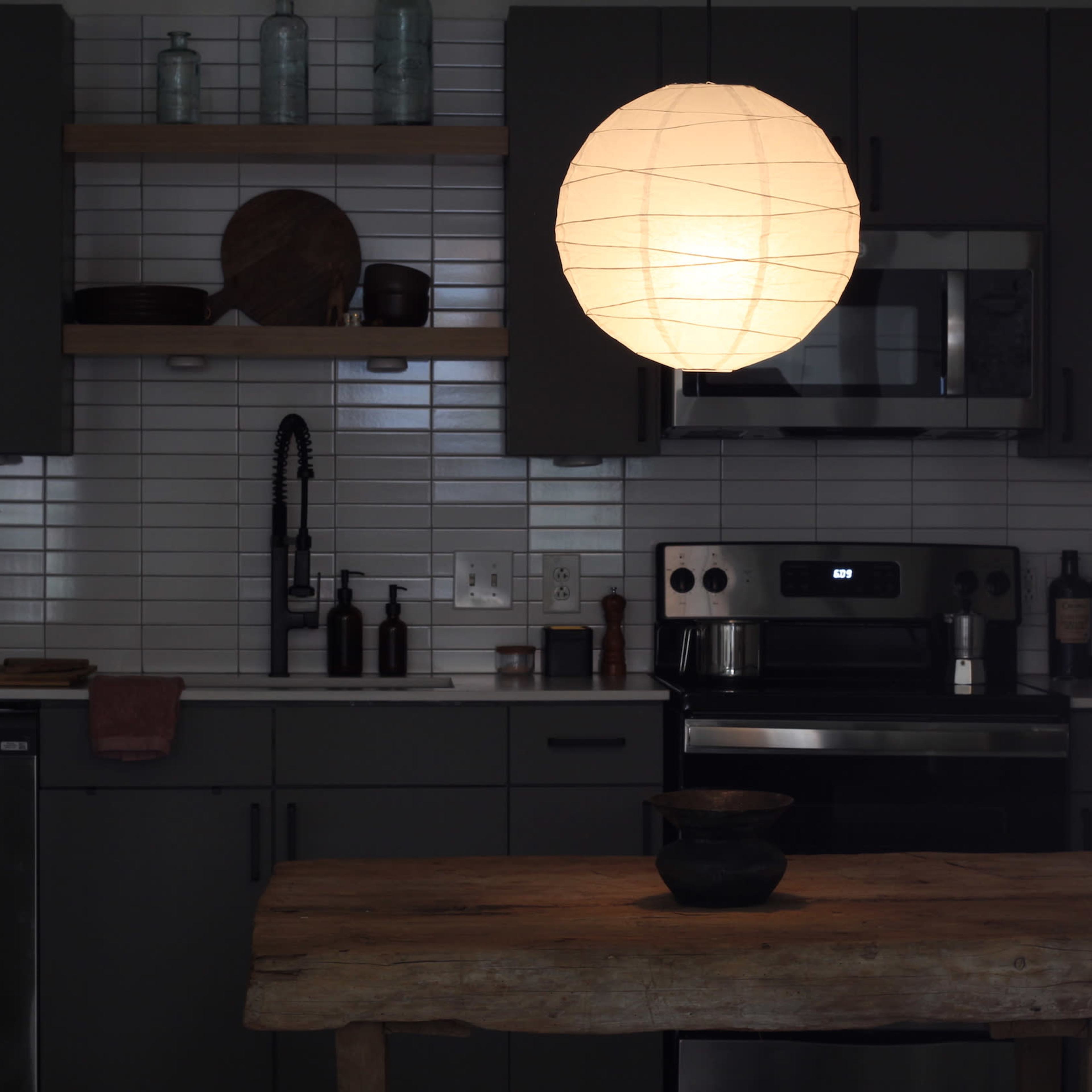 A pendant light hangs above a wooden table in a modern kitchen with gray cabinetry and stainless steel appliances.