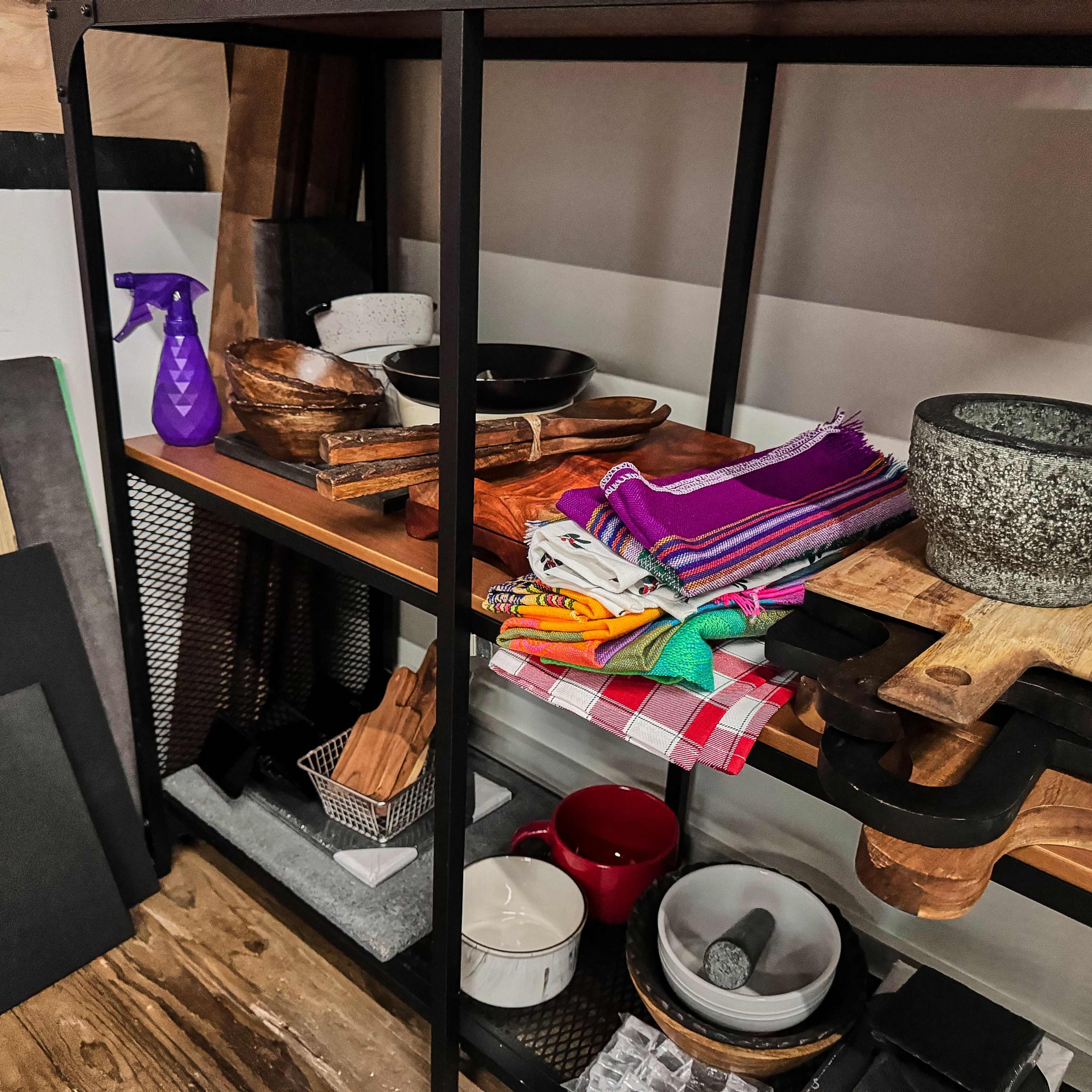 A shelving unit displays a variety of kitchen items, including bowls, cutting boards, colorful textiles, and cleaning supplies.