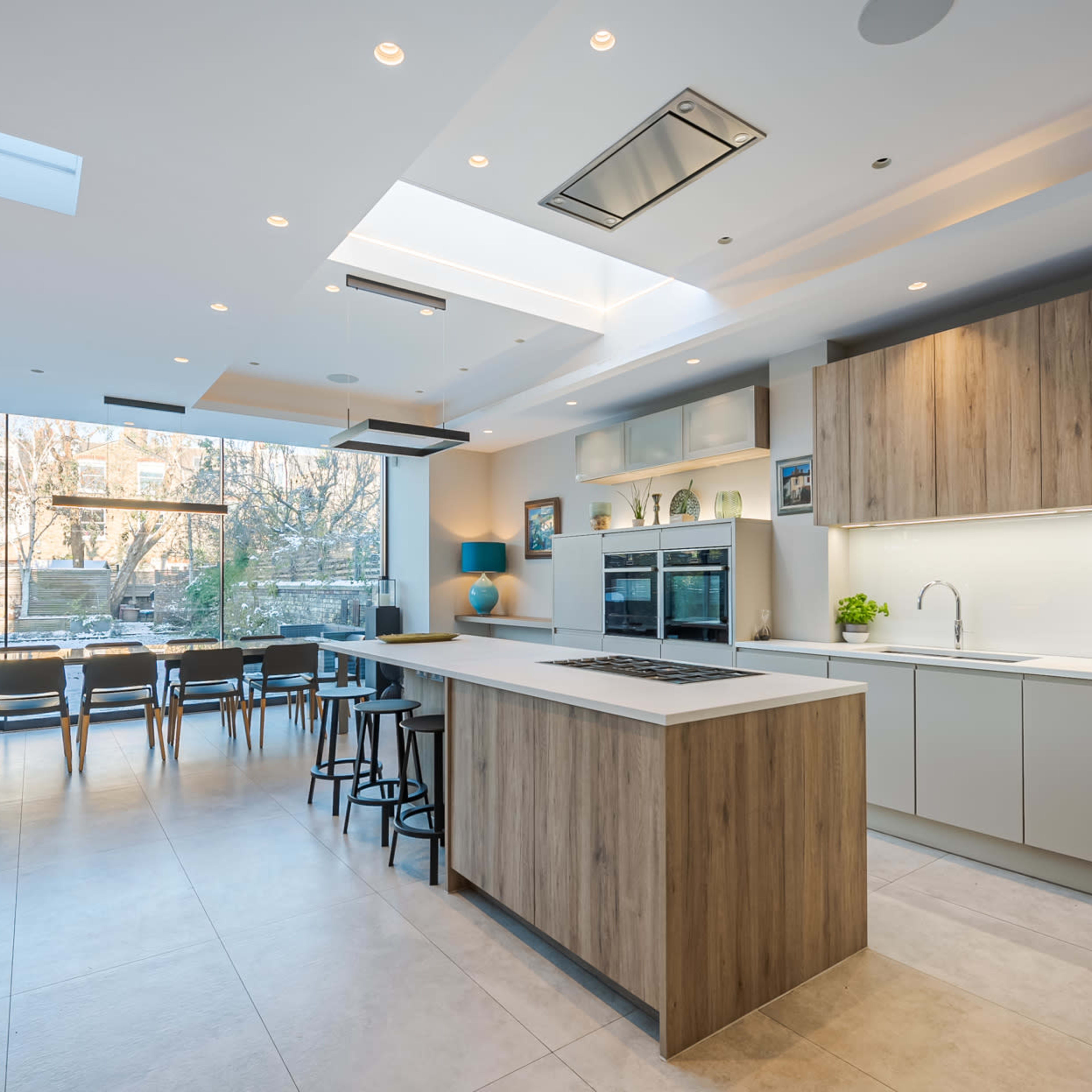 A modern kitchen with an island, sleek cabinetry, and a large window overlooking an outdoor dining area.