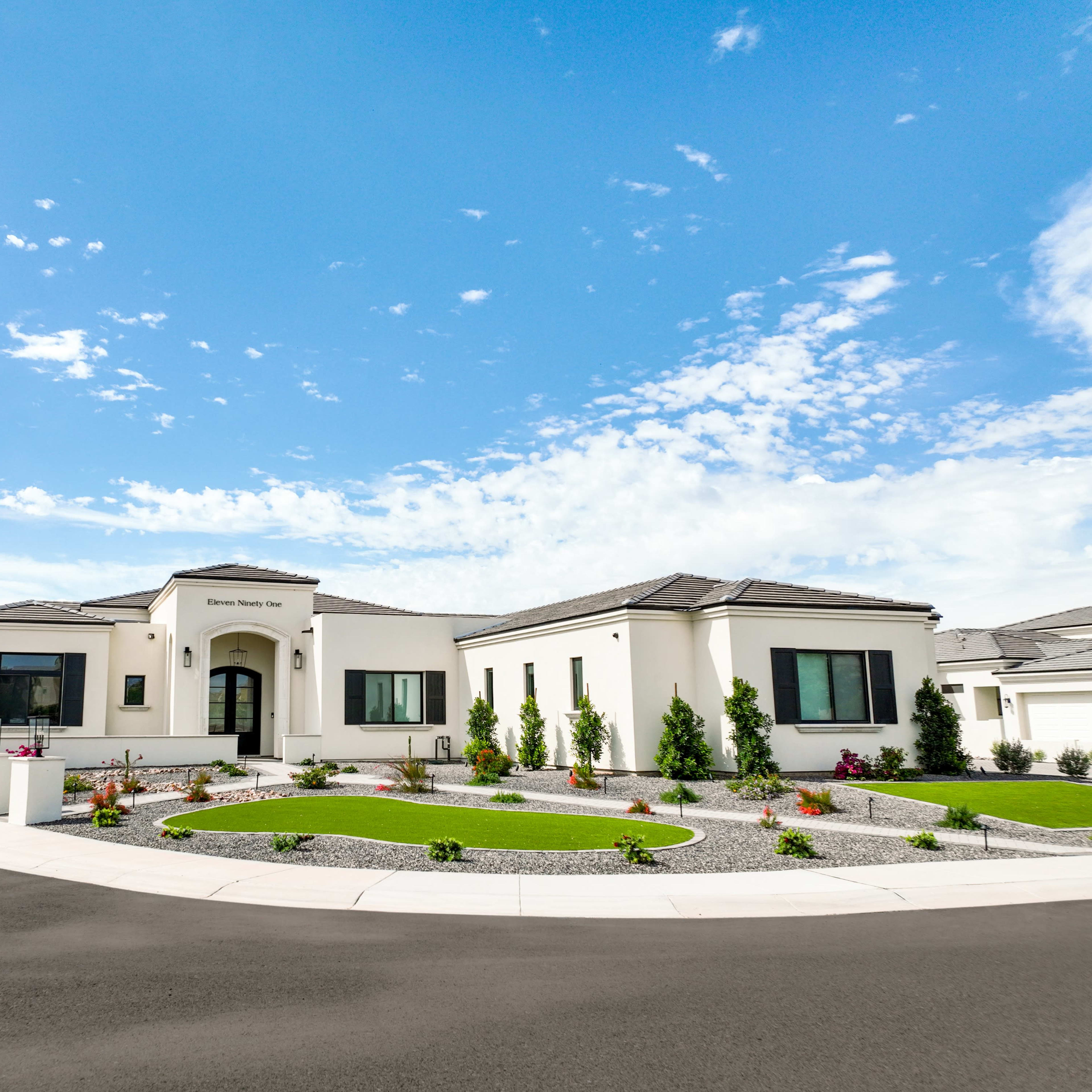 A modern single-story house features a spacious front yard with landscaped gardens and a circular driveway under a clear blue sky.