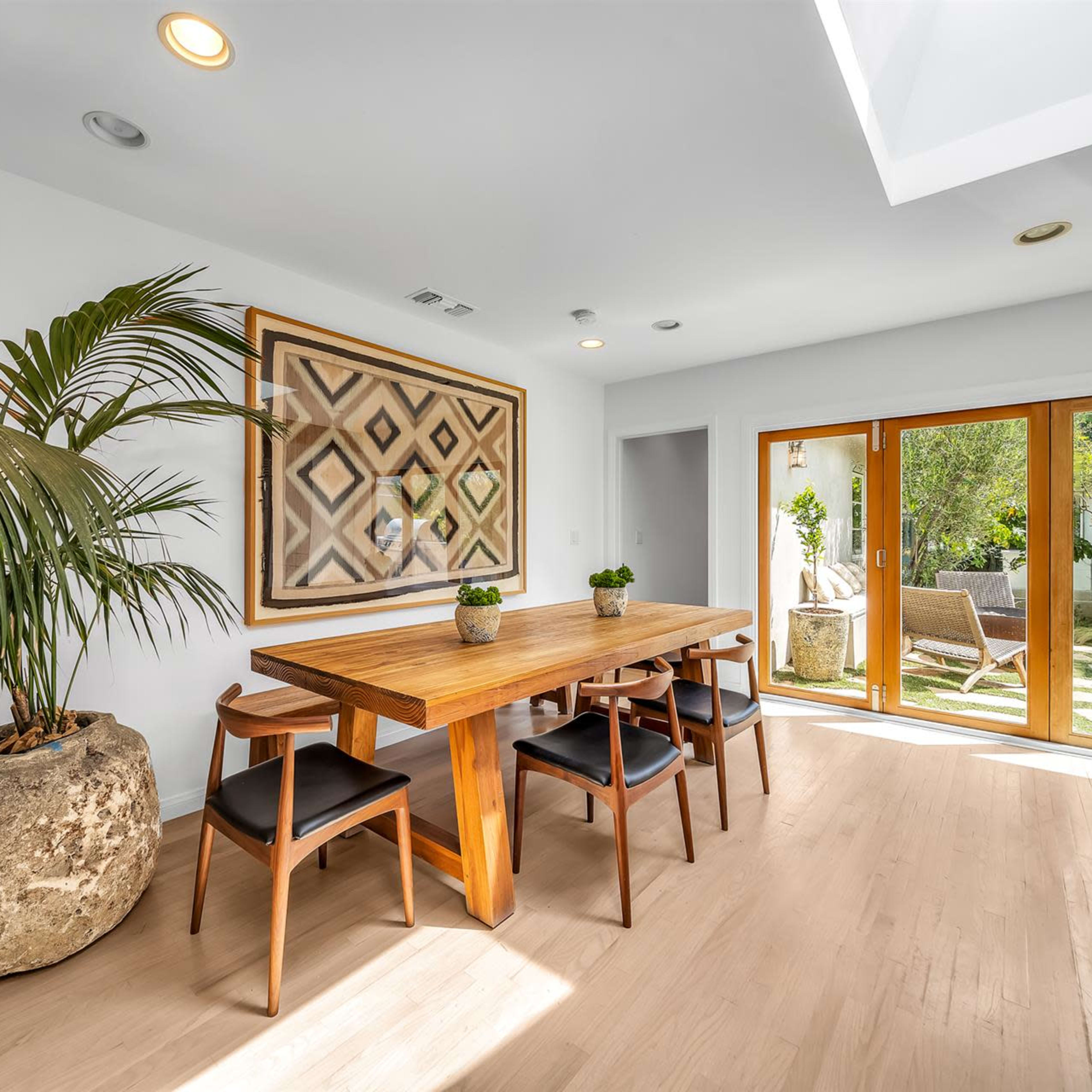 A dining area features a wooden table surrounded by black chairs, with sliding glass doors opening to a garden.