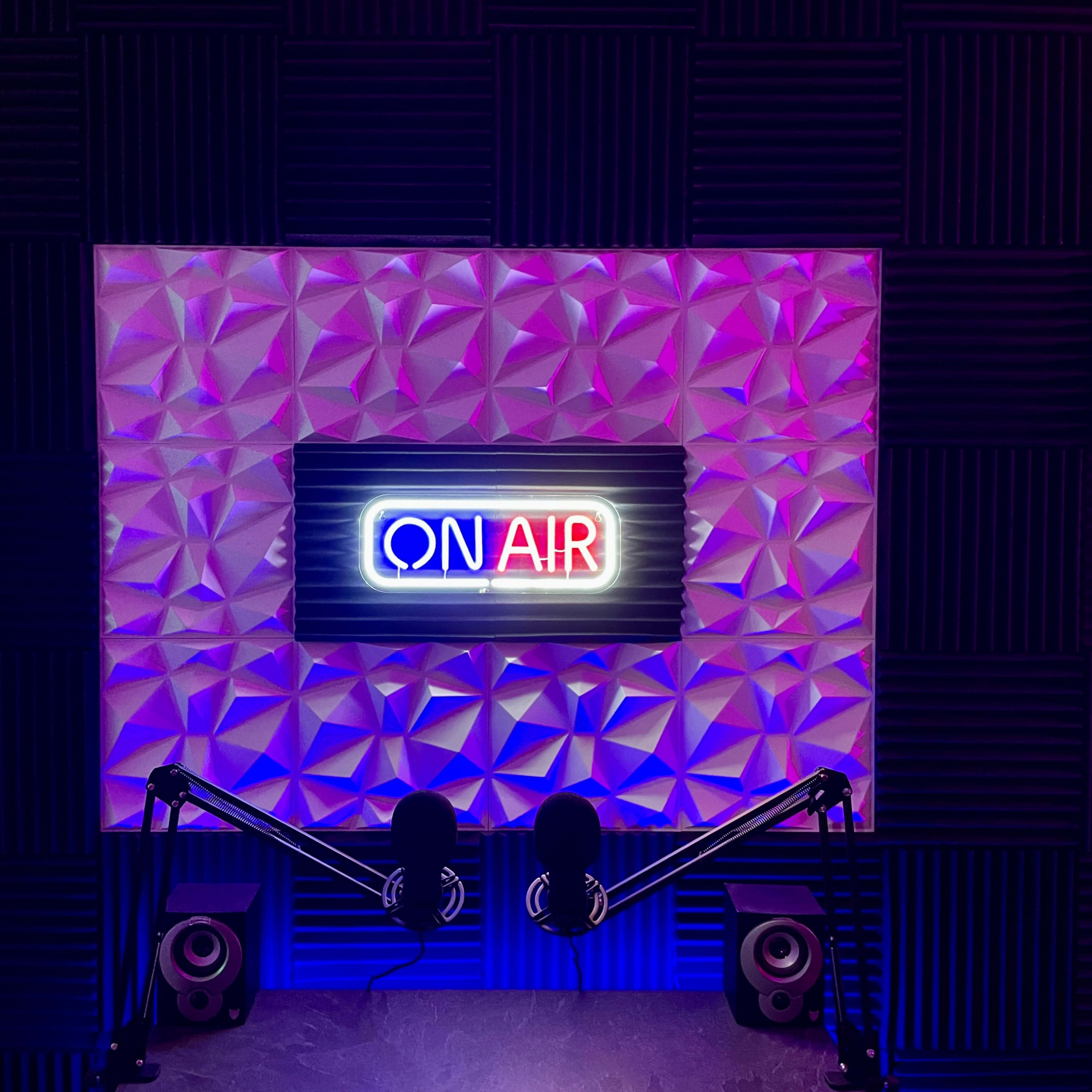 A studio setup featuring a "ON AIR" neon sign against a textured wall, with two microphones and speakers positioned below it.