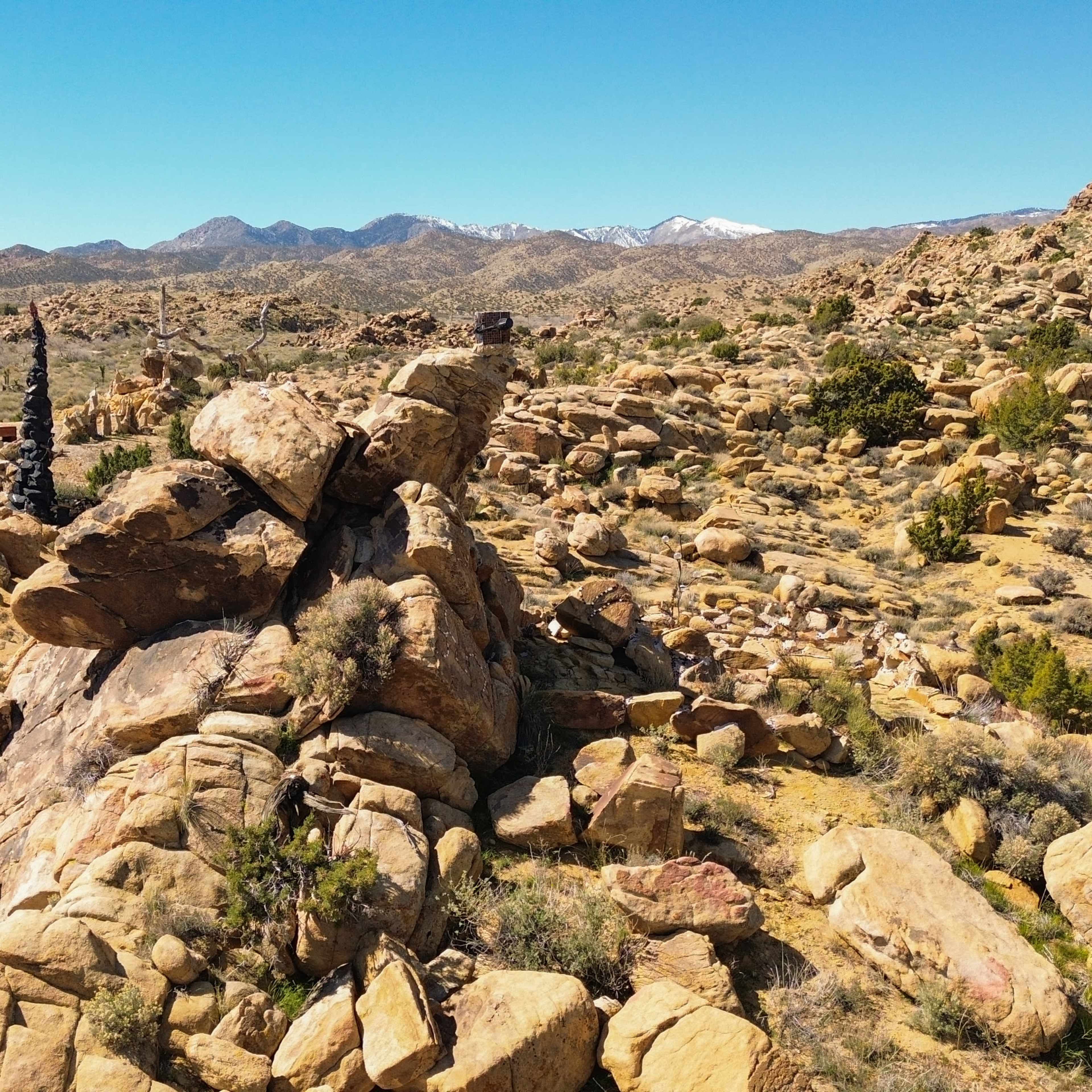 A rugged landscape features large boulders amidst sparse vegetation and distant mountains.