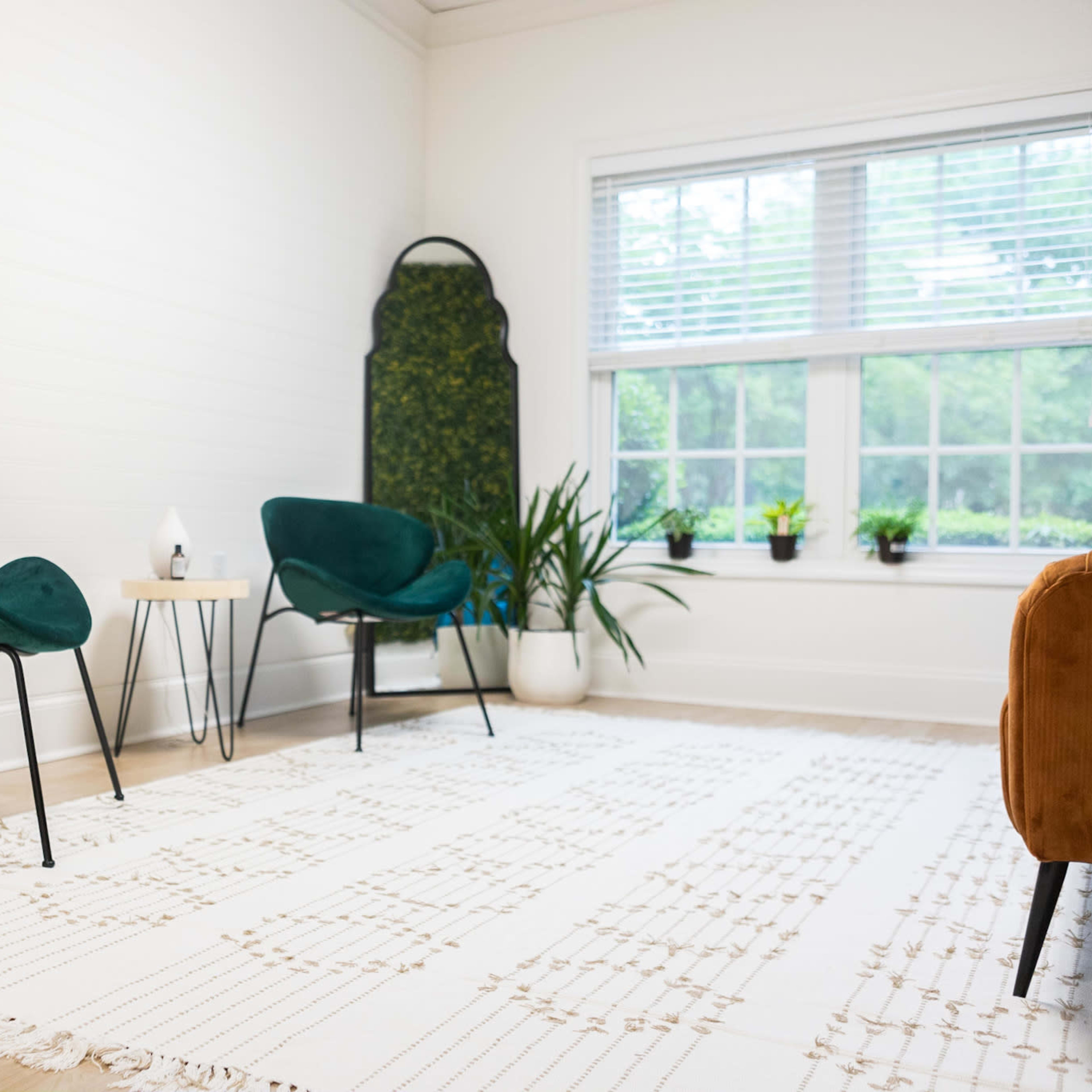 A bright room with two green chairs, a small table, a potted plant, and a large window with natural light.