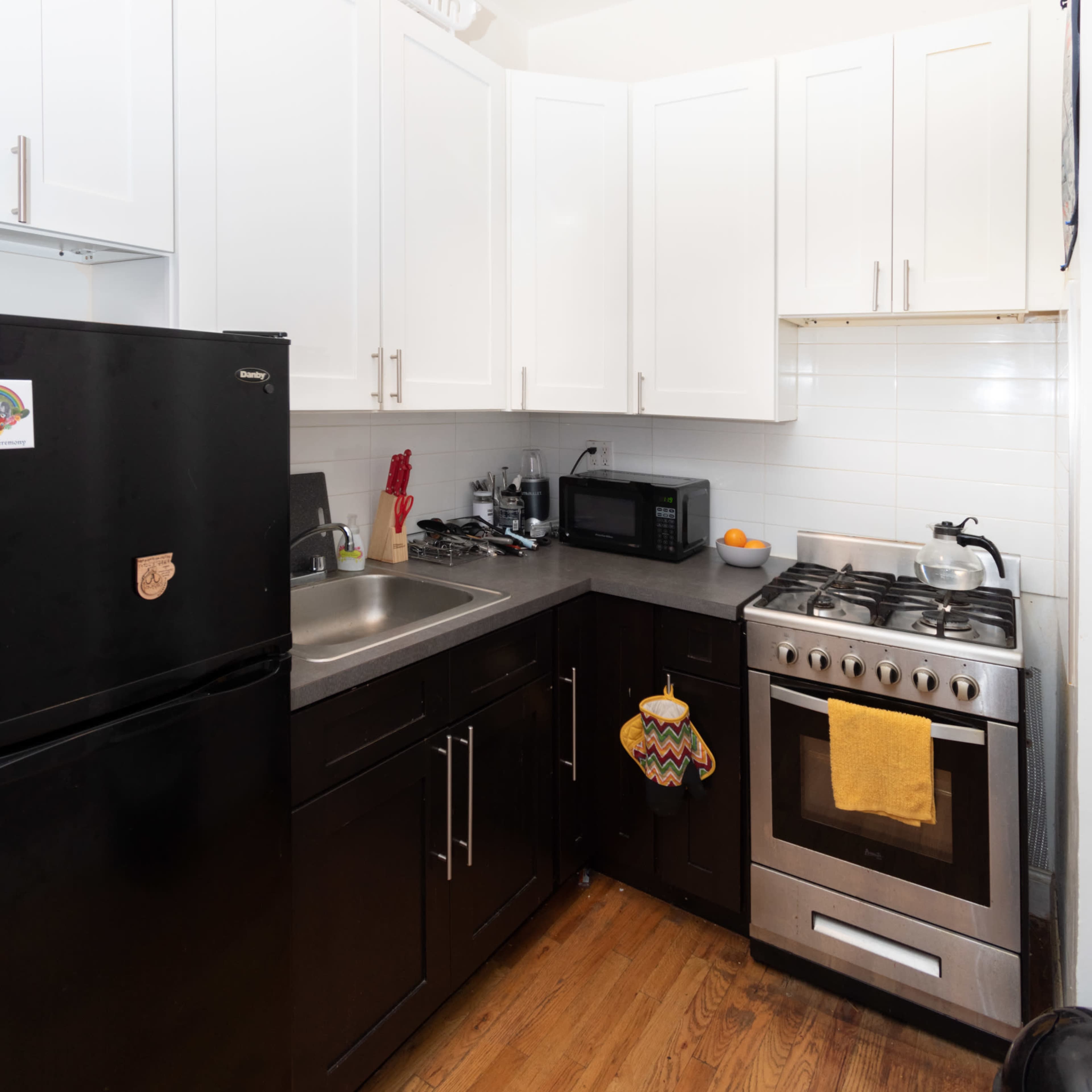 A compact kitchen with white cabinets, stainless steel appliances, and wooden flooring.