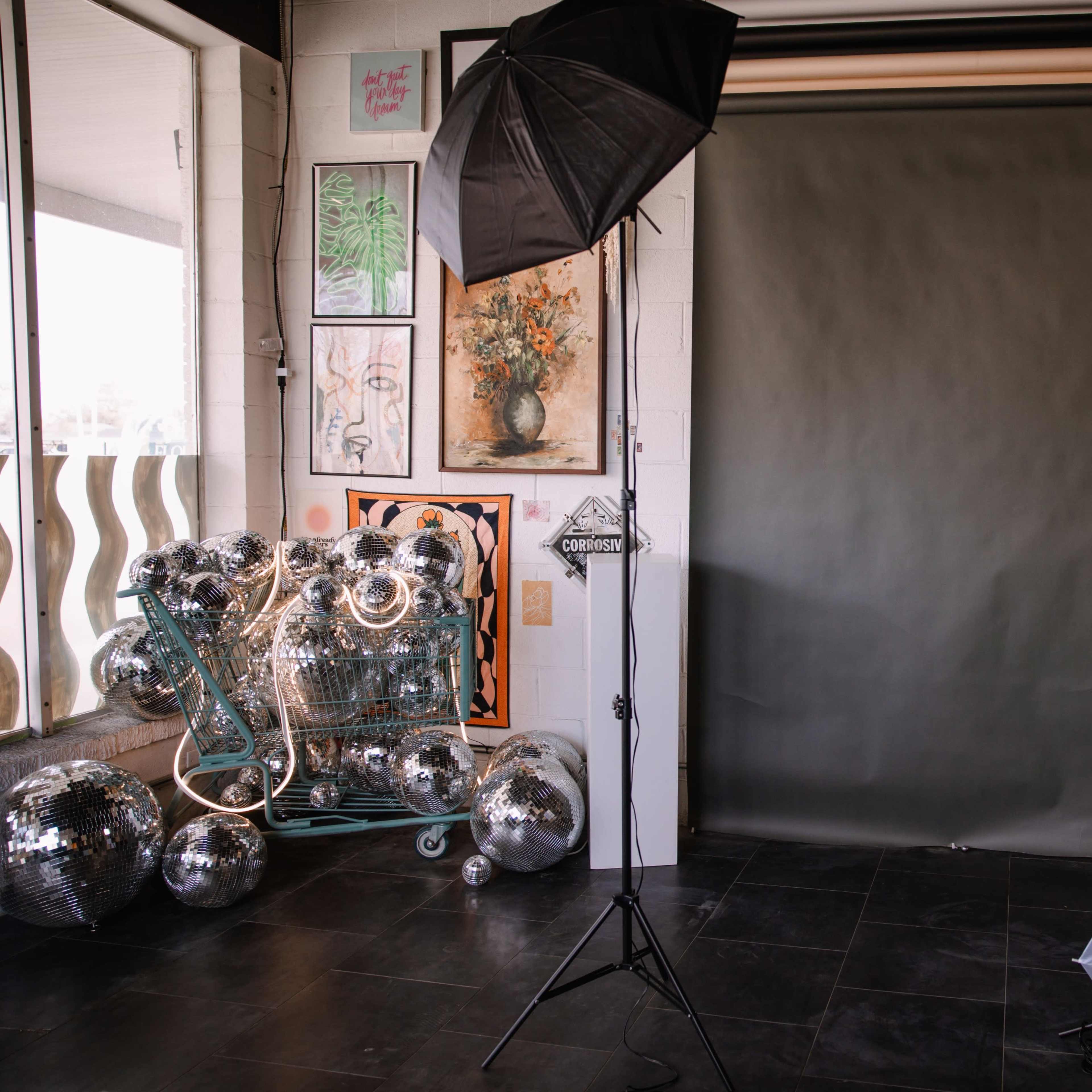 A photography studio with a gray backdrop, lighting equipment, and several disco balls piled in a cart.
