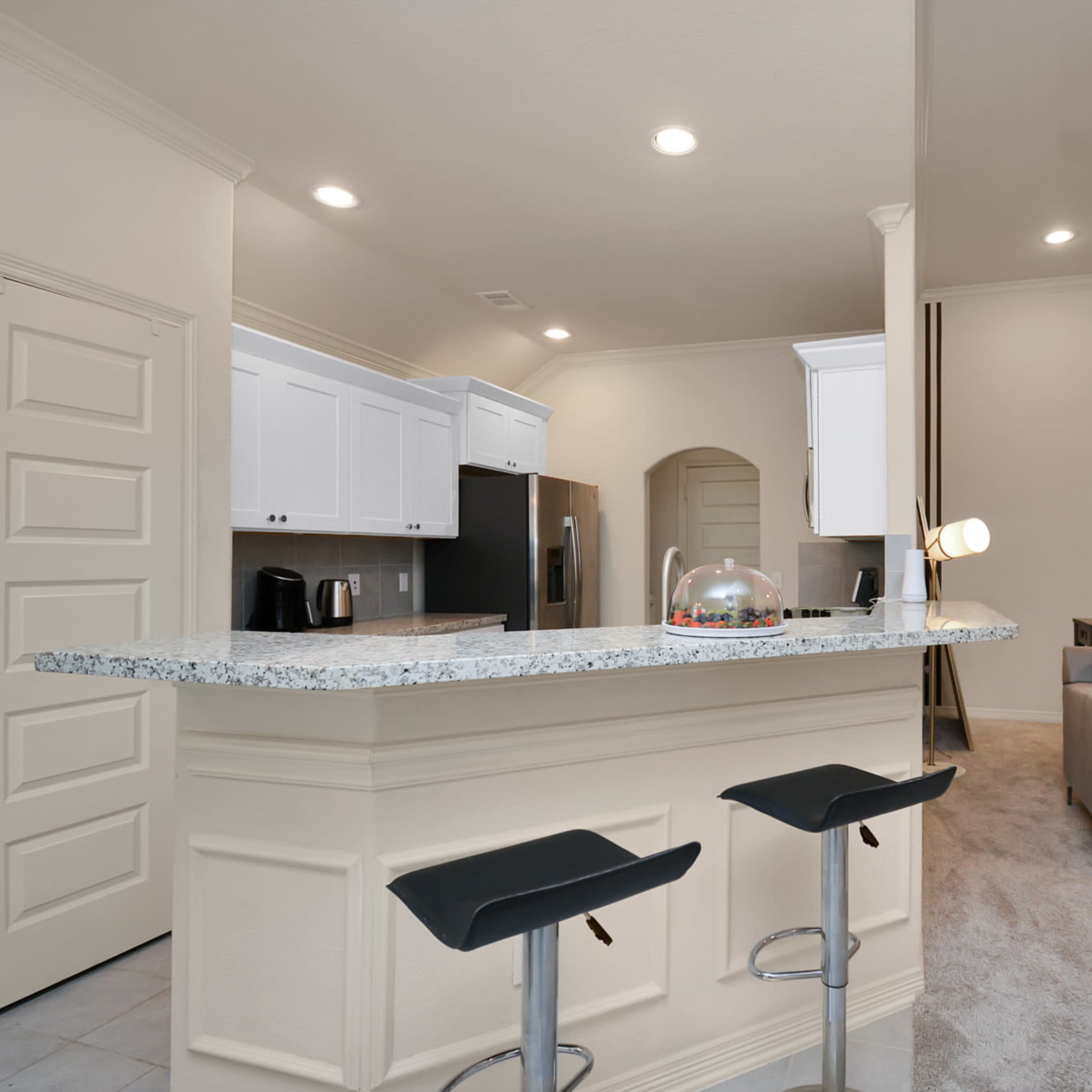 A modern kitchen with a gray countertop, white cabinets, and bar seating adjacent to a living area featuring a gray couch.
