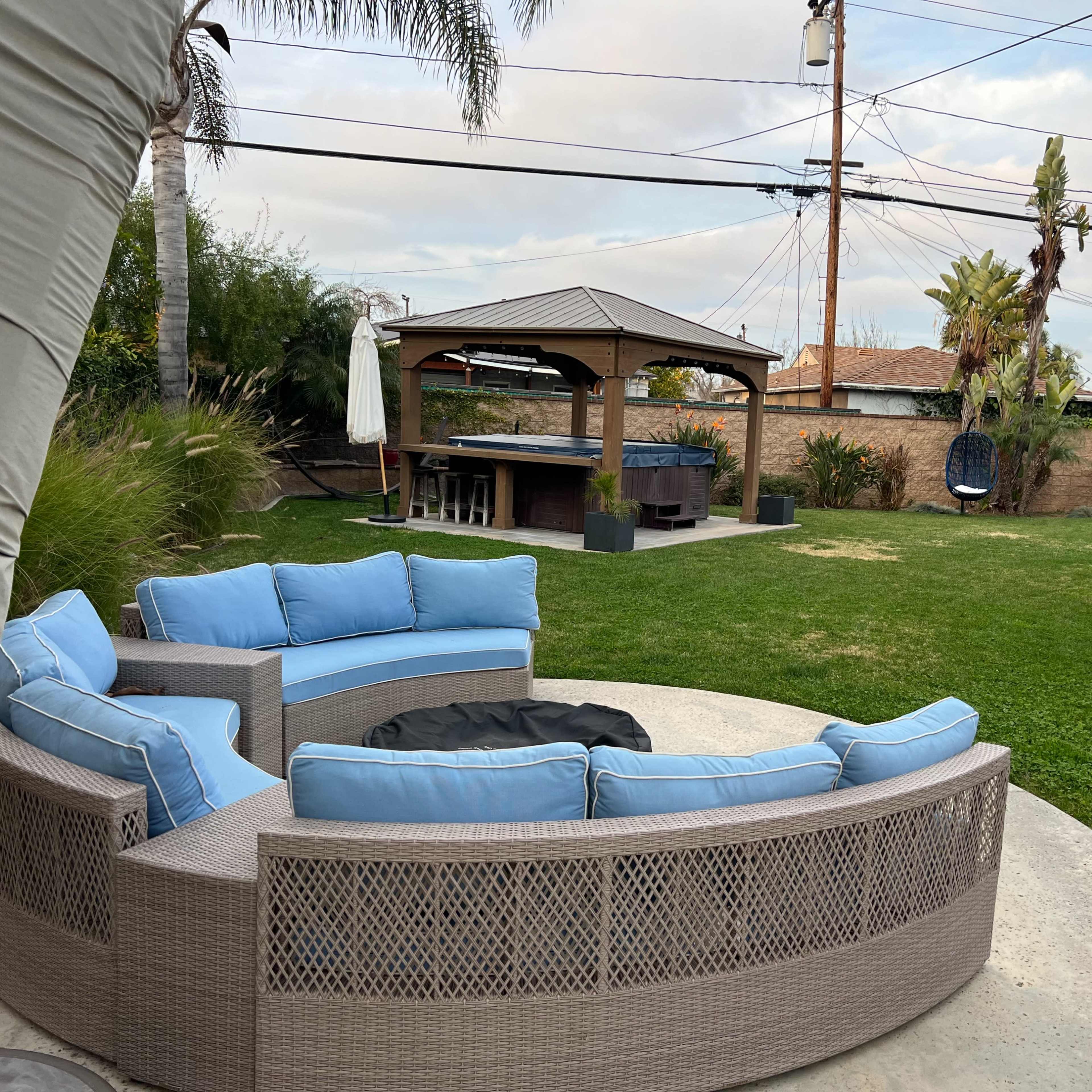 A backyard featuring a circular sectional sofa with blue cushions, a gazebo, and a well-maintained lawn with palm trees.