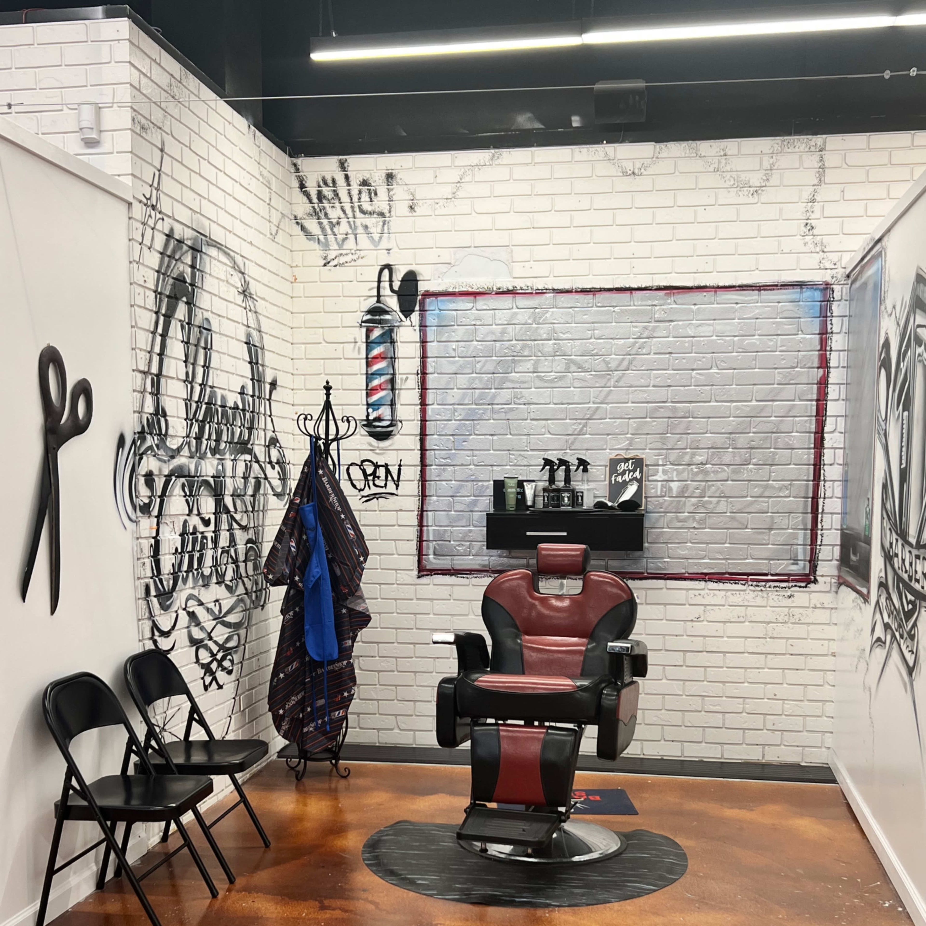 A modern barber shop interior with a red barber chair, a wall decorated with graffiti-style art, and a waiting area featuring black folding chairs.