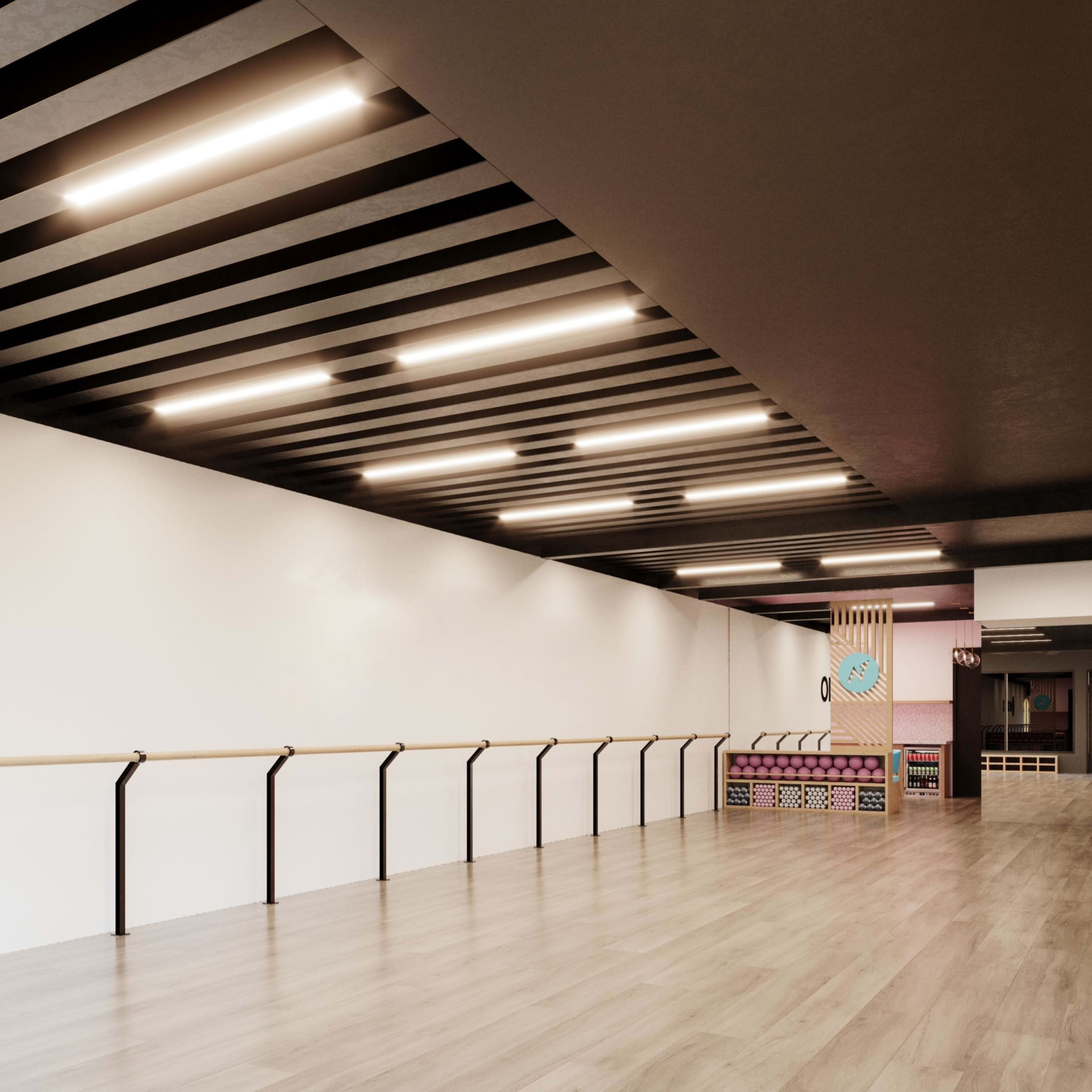 A spacious, empty dance studio with wooden floors, a ballet barre along one wall, and overhead lighting.