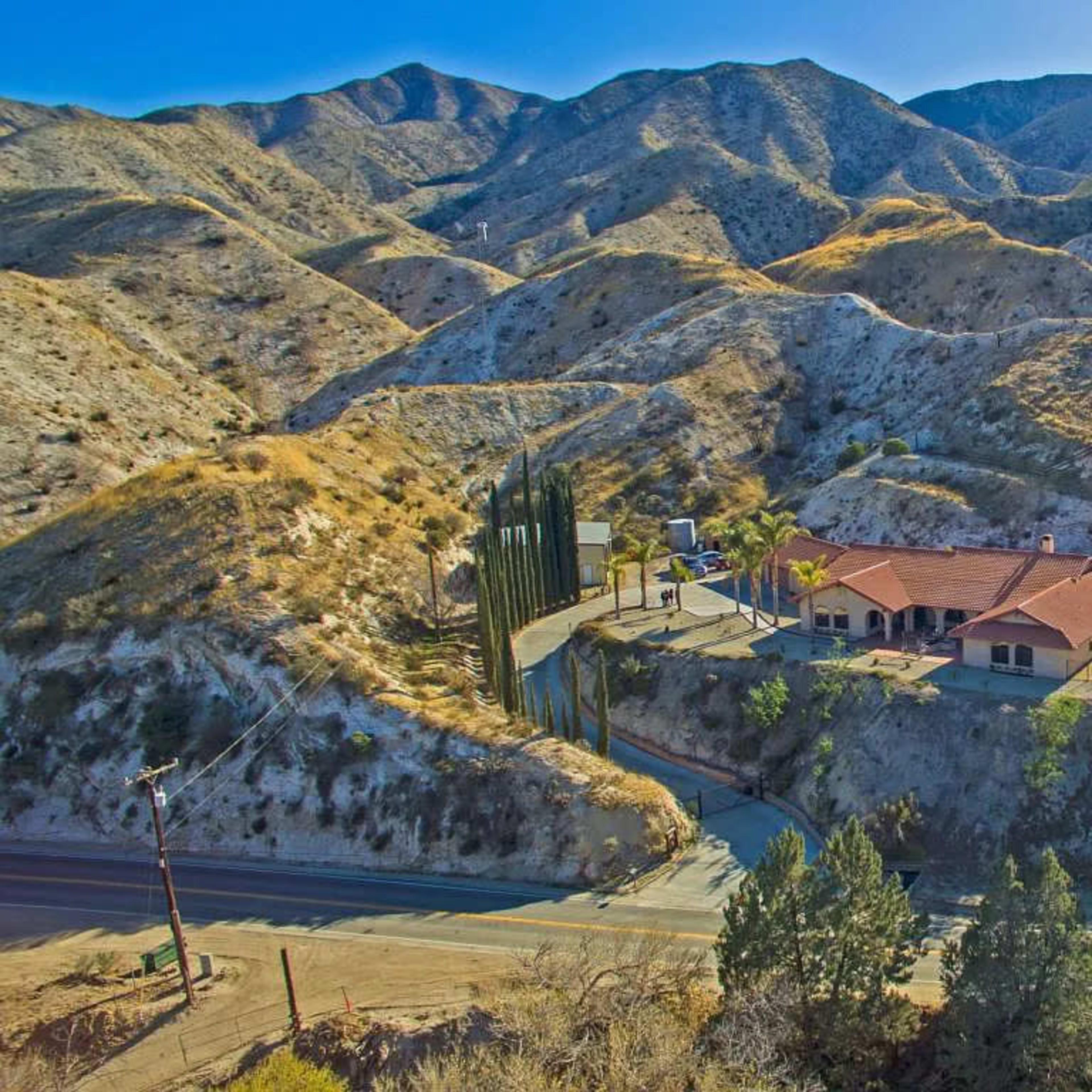 A house with a swimming pool is located on a hillside surrounded by mountains and sparse vegetation.