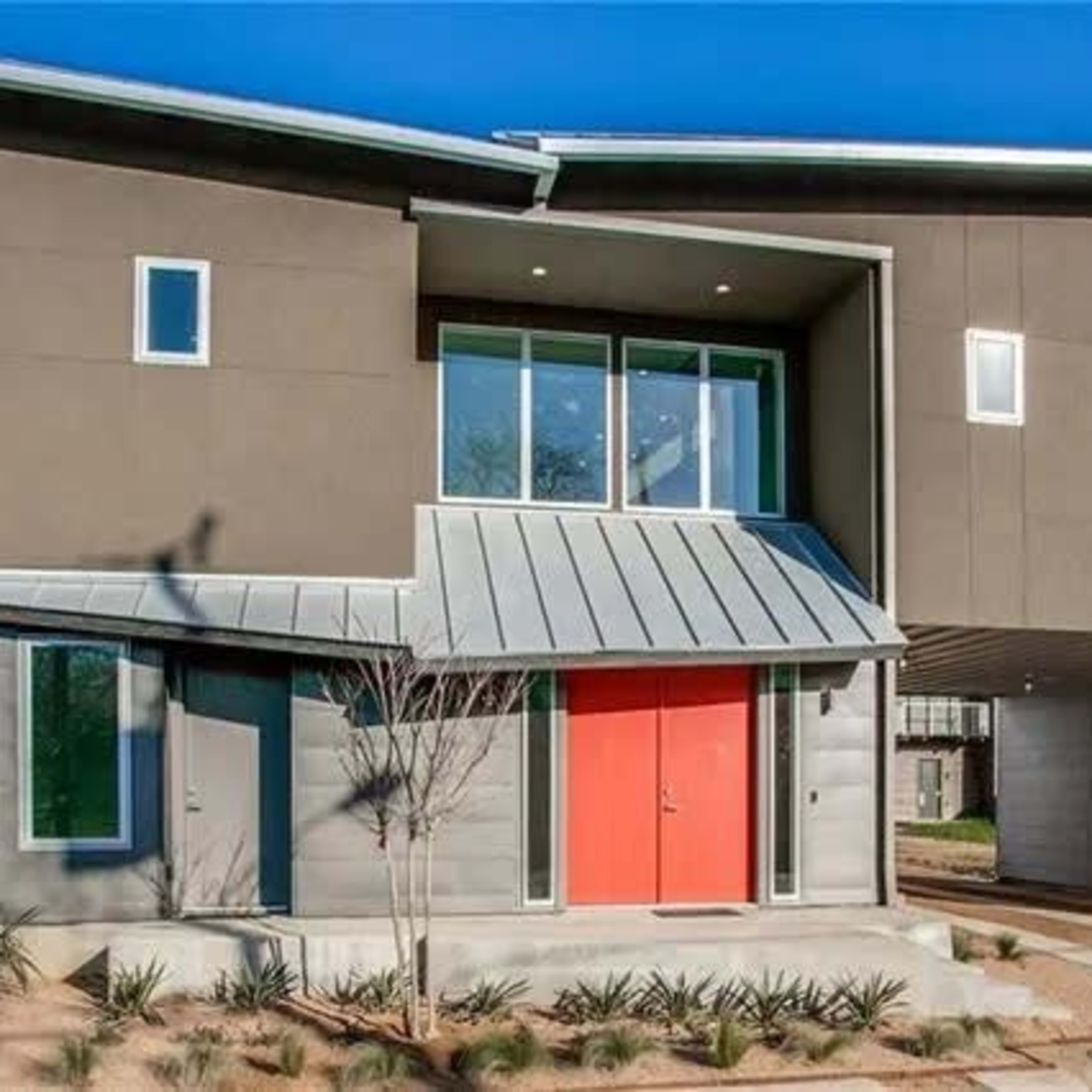 A modern two-story house features a unique angular design with a metal roof and bright red front doors.