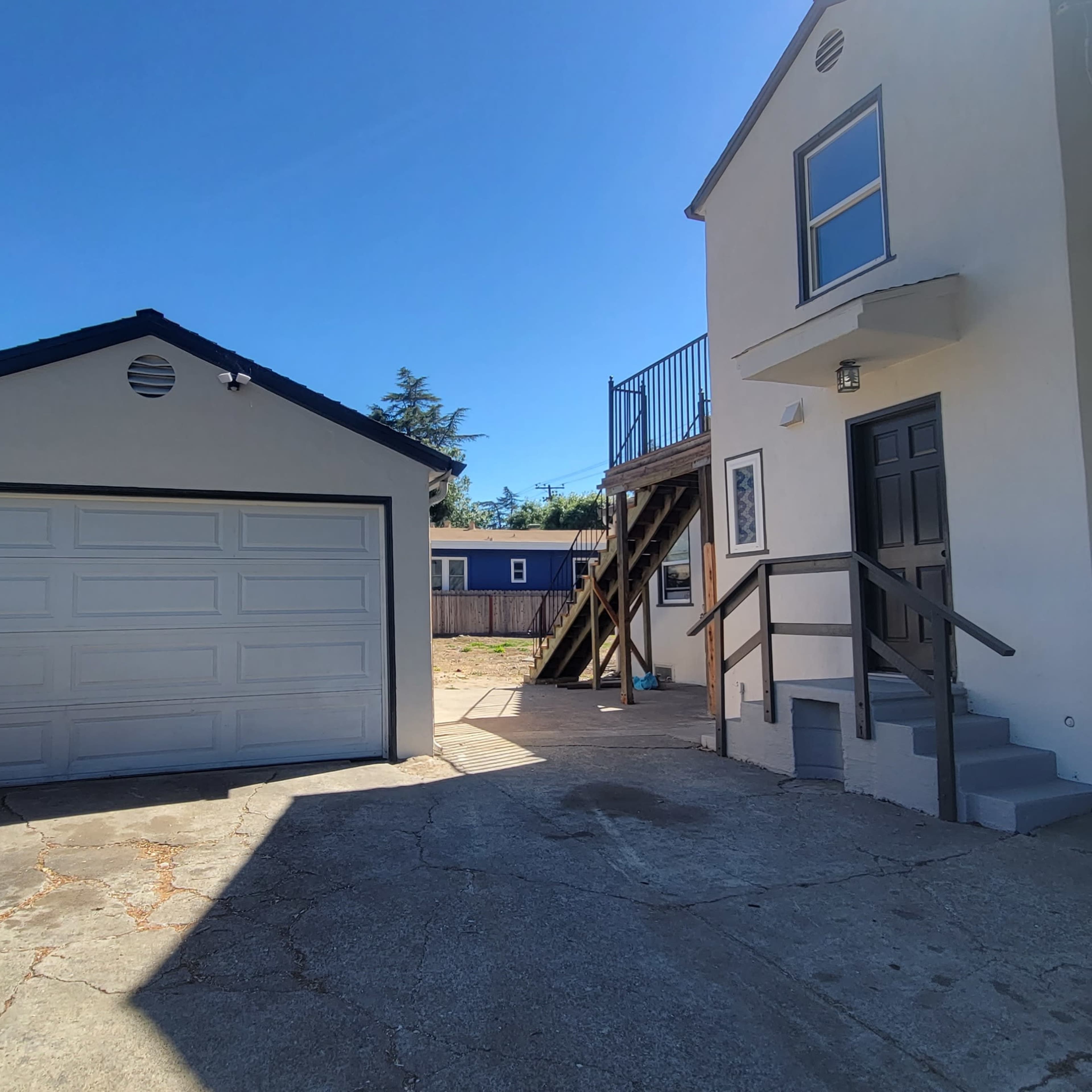 A residential area with a two-story house on the right, a garage on the left, and a paved driveway leading between them.