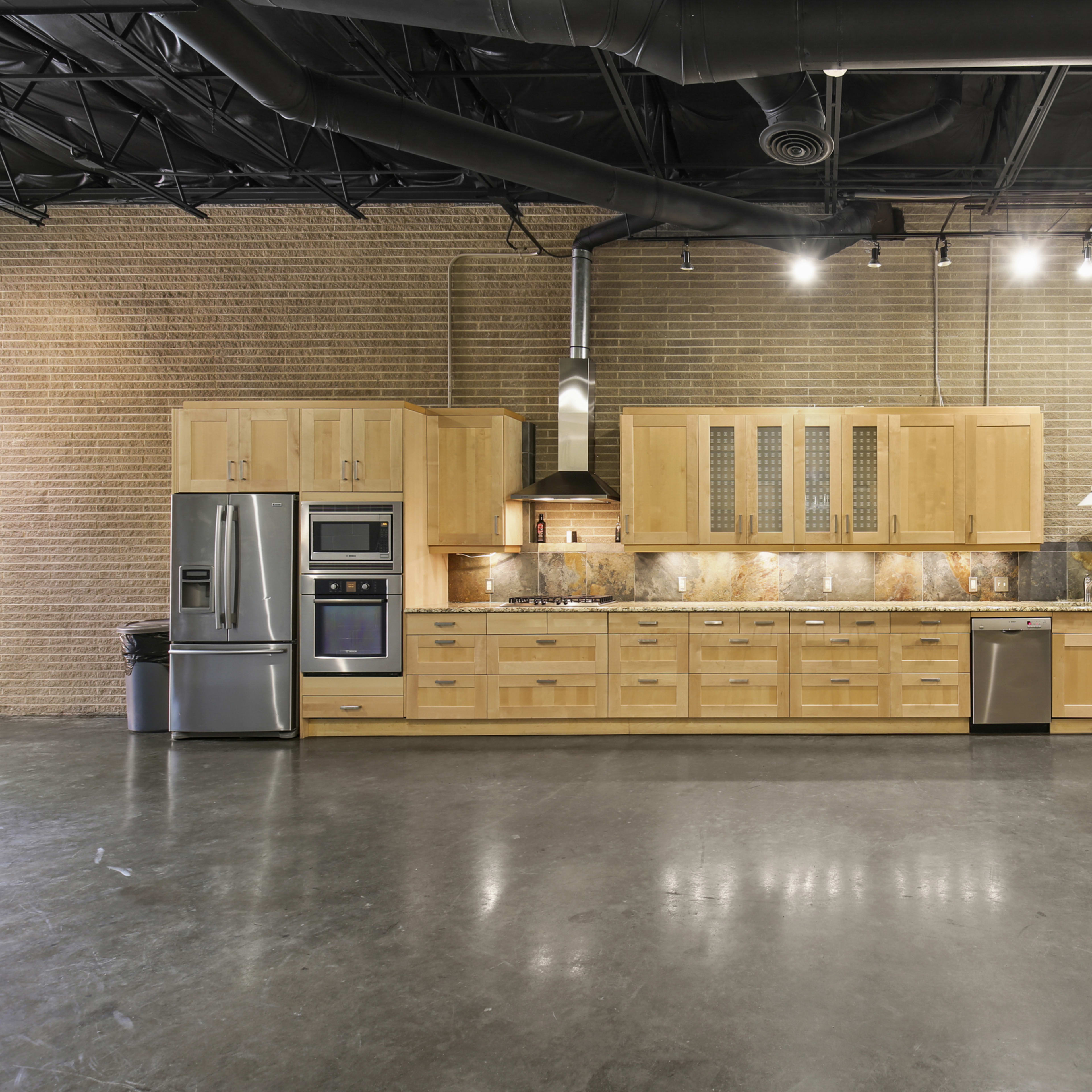 A large kitchen with wooden cabinetry, stainless steel appliances, and a granite countertop in a modern industrial space.