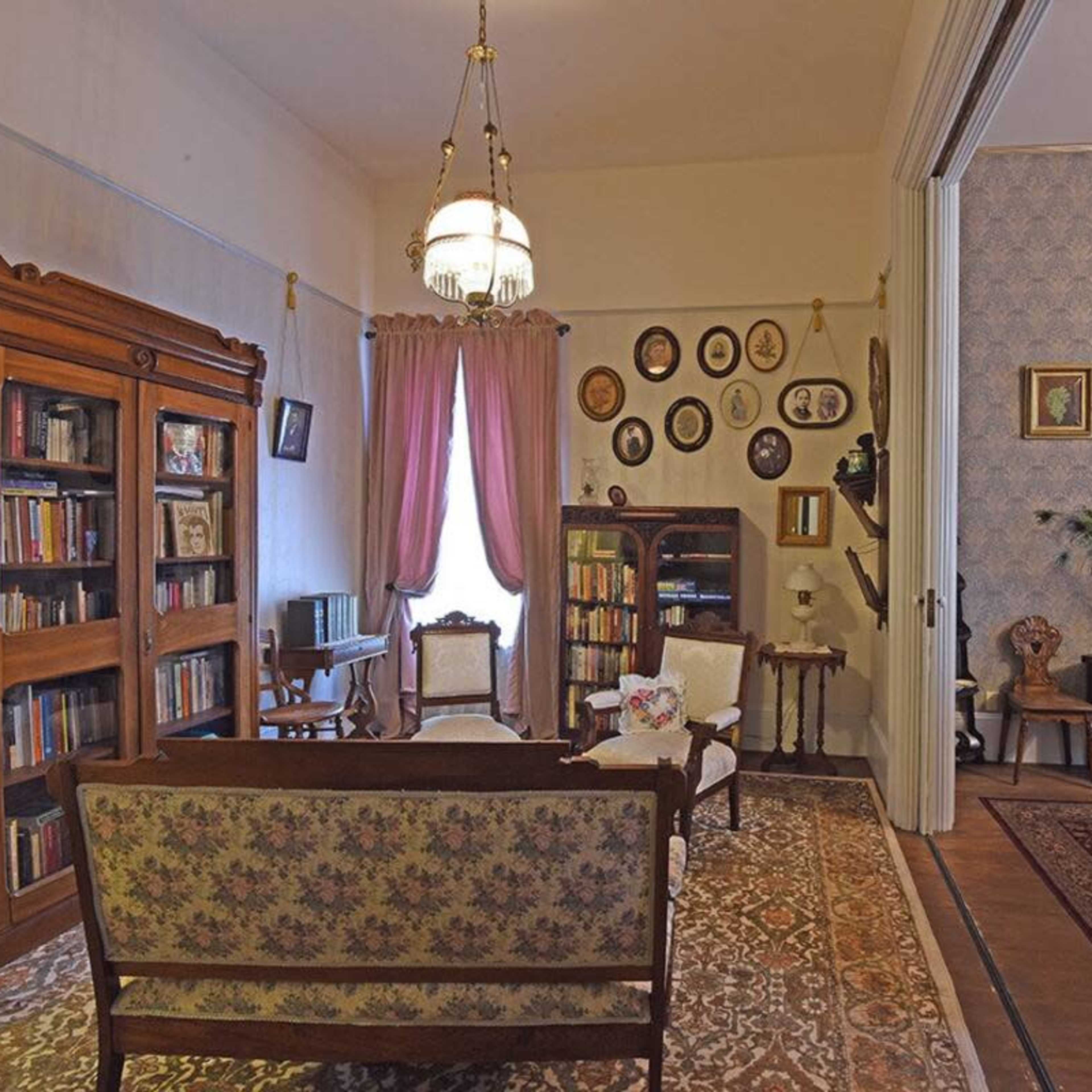 A vintage living room with a bookshelf, a floral-patterned sofa, and framed pictures hanging on the wall.