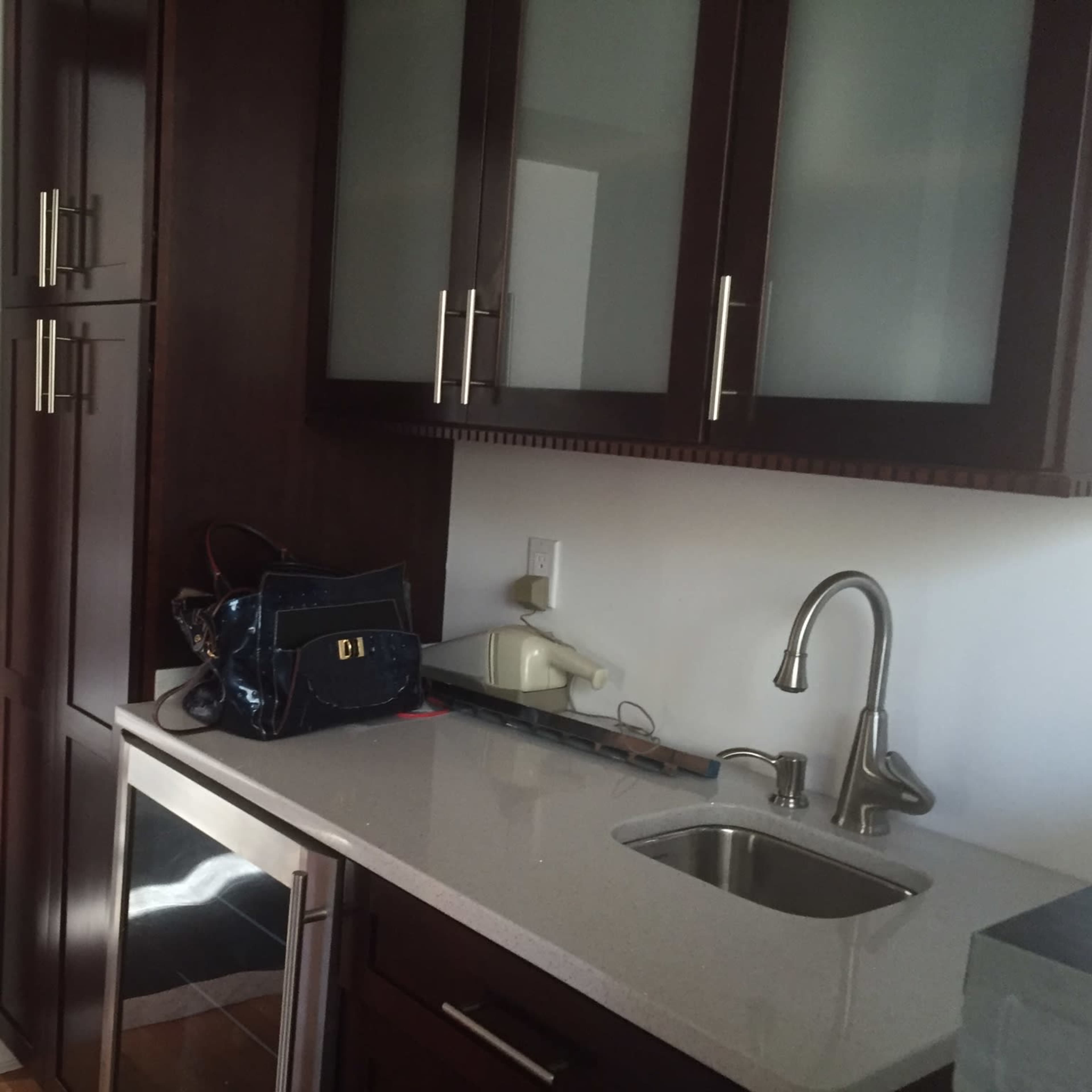 A modern kitchen area with dark wood cabinets, a countertop, a sink, and a doorway leading to another room.