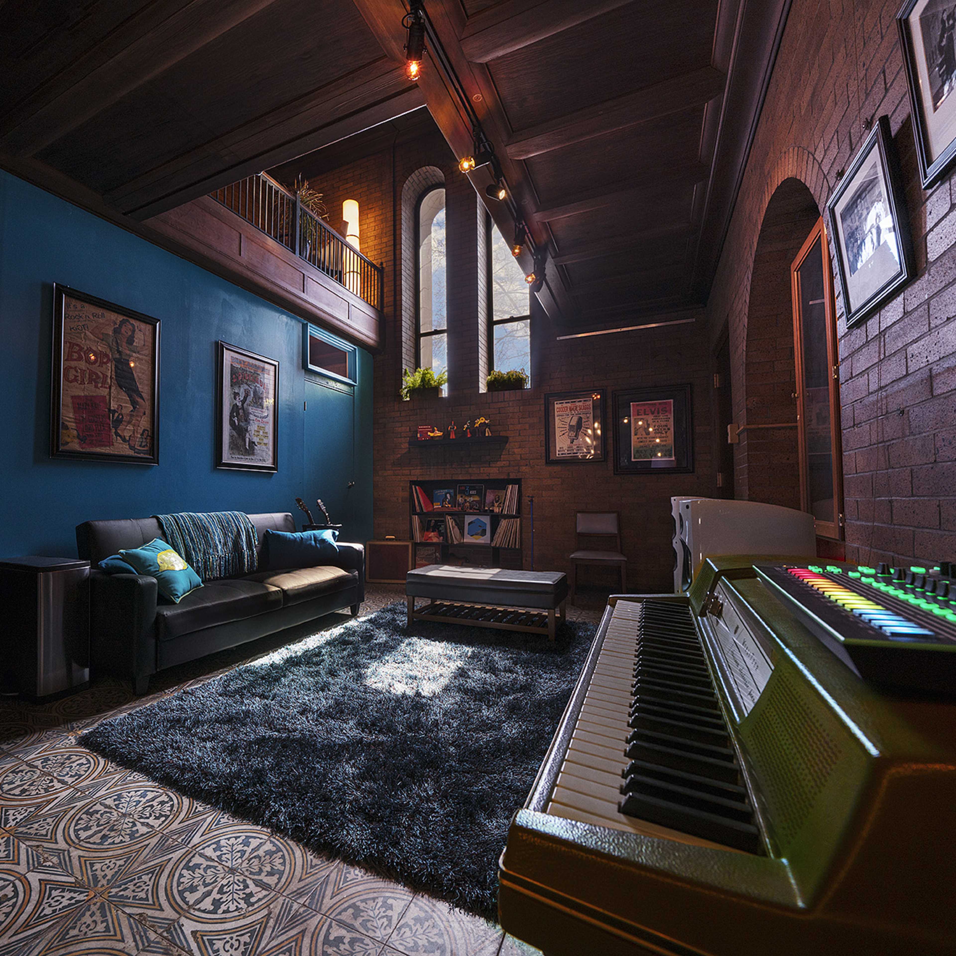 A stylish living room featuring a sofa, a coffee table on a patterned rug, and a vintage keyboard positioned in the foreground, with large windows illuminating the space.