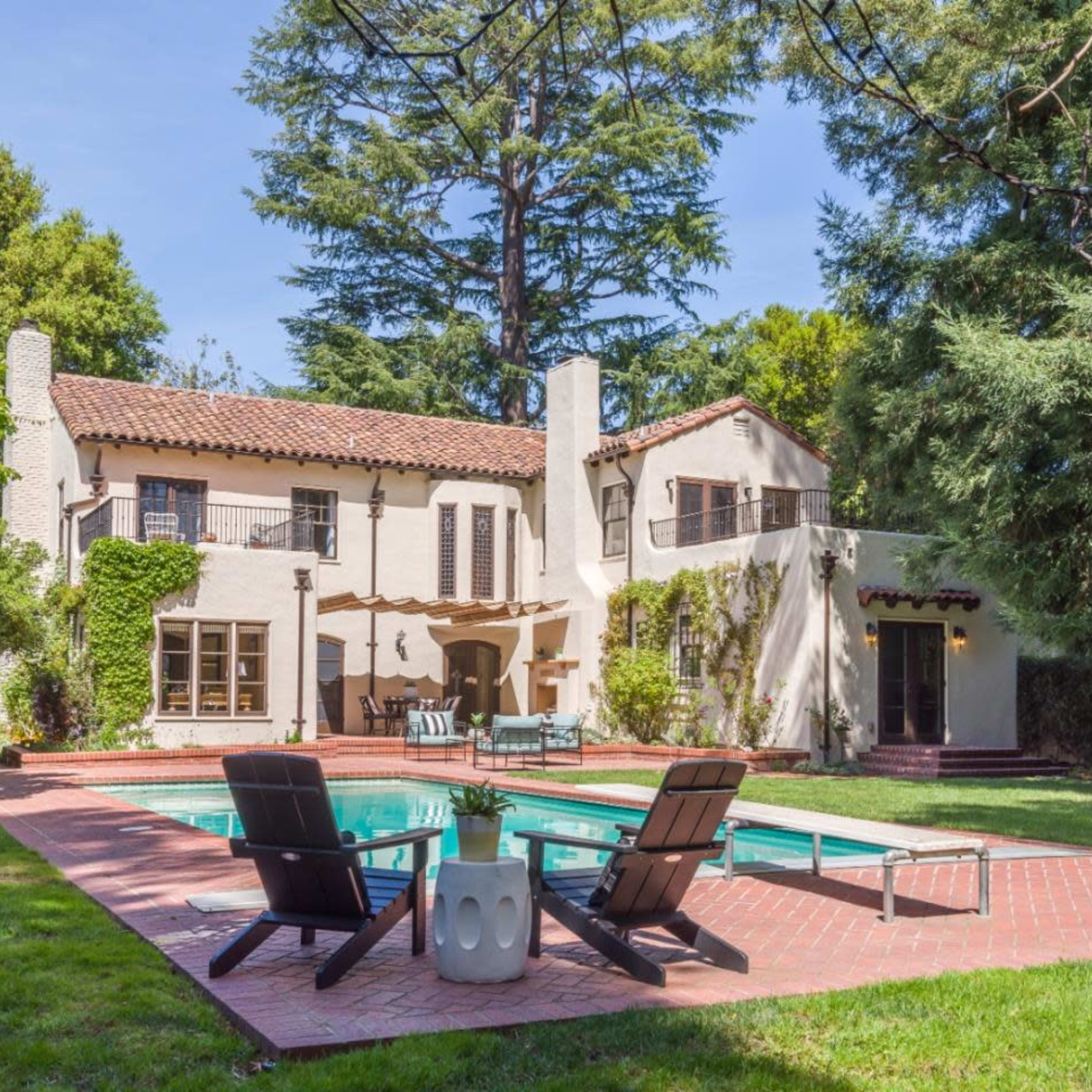A two-story house with a tiled roof and a swimming pool surrounded by lounge chairs in a landscaped backyard.