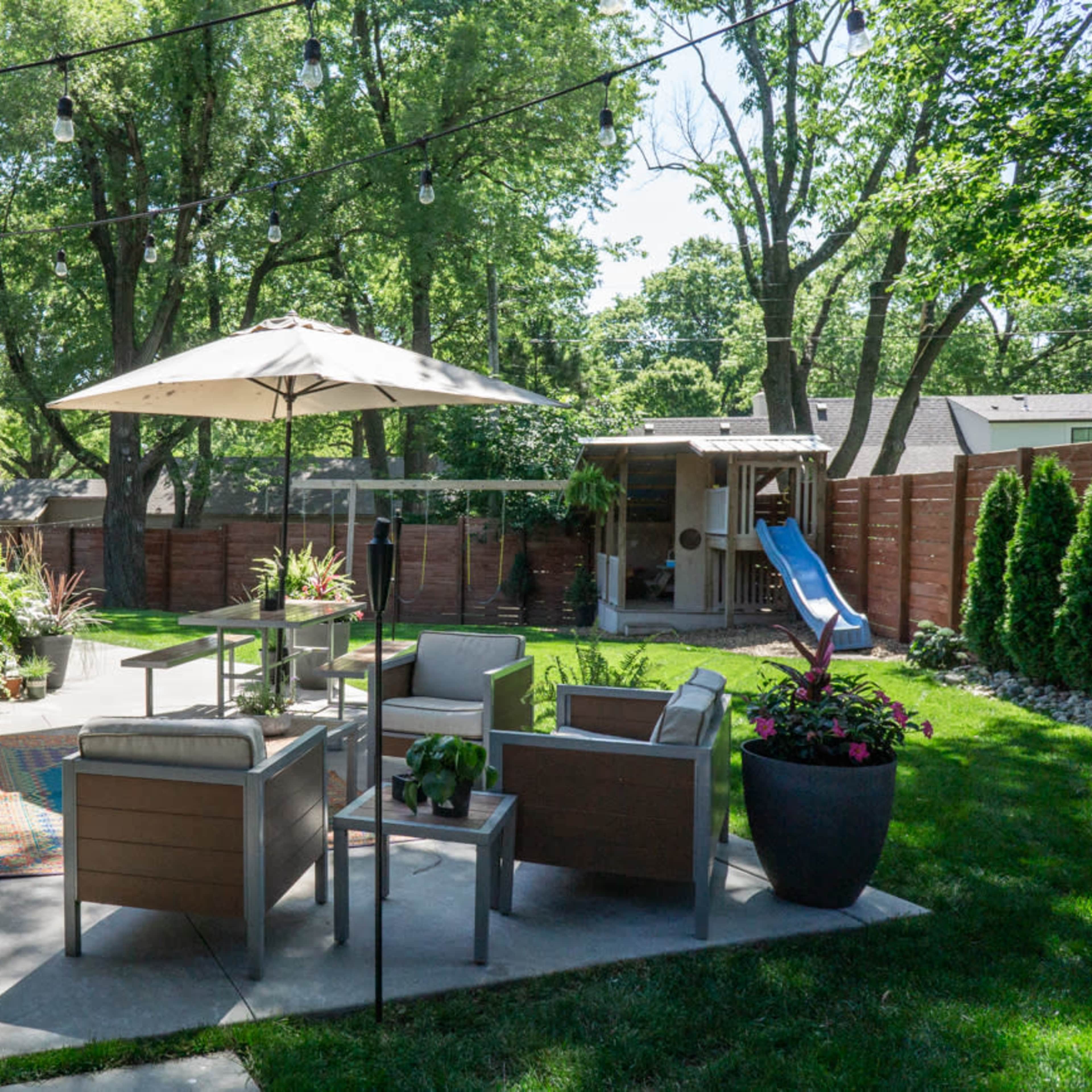 A well-maintained backyard patio with modern outdoor furniture, an umbrella, and lush greenery surrounding the area.