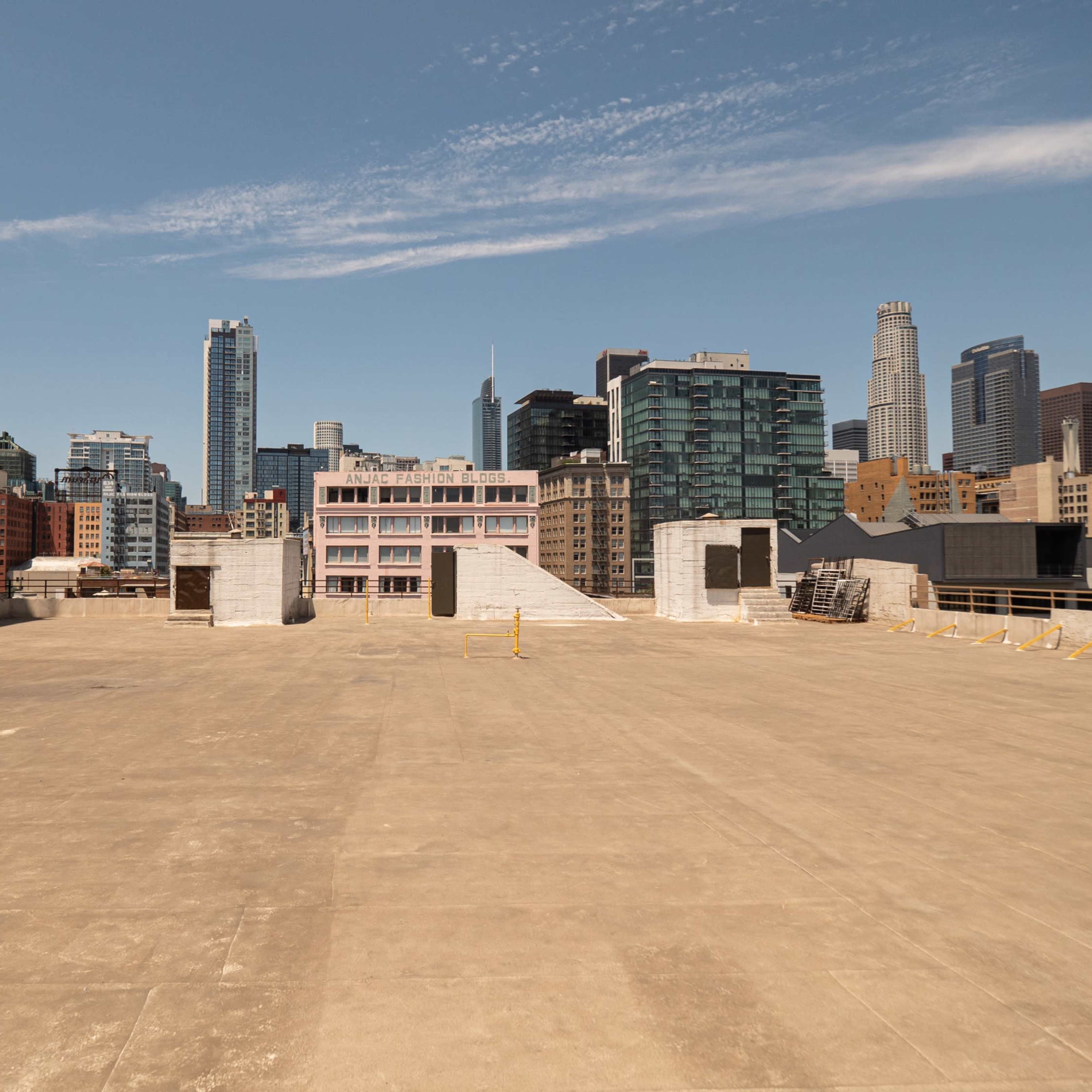A vast, empty rooftop overlooks a city skyline filled with tall buildings and a clear blue sky.