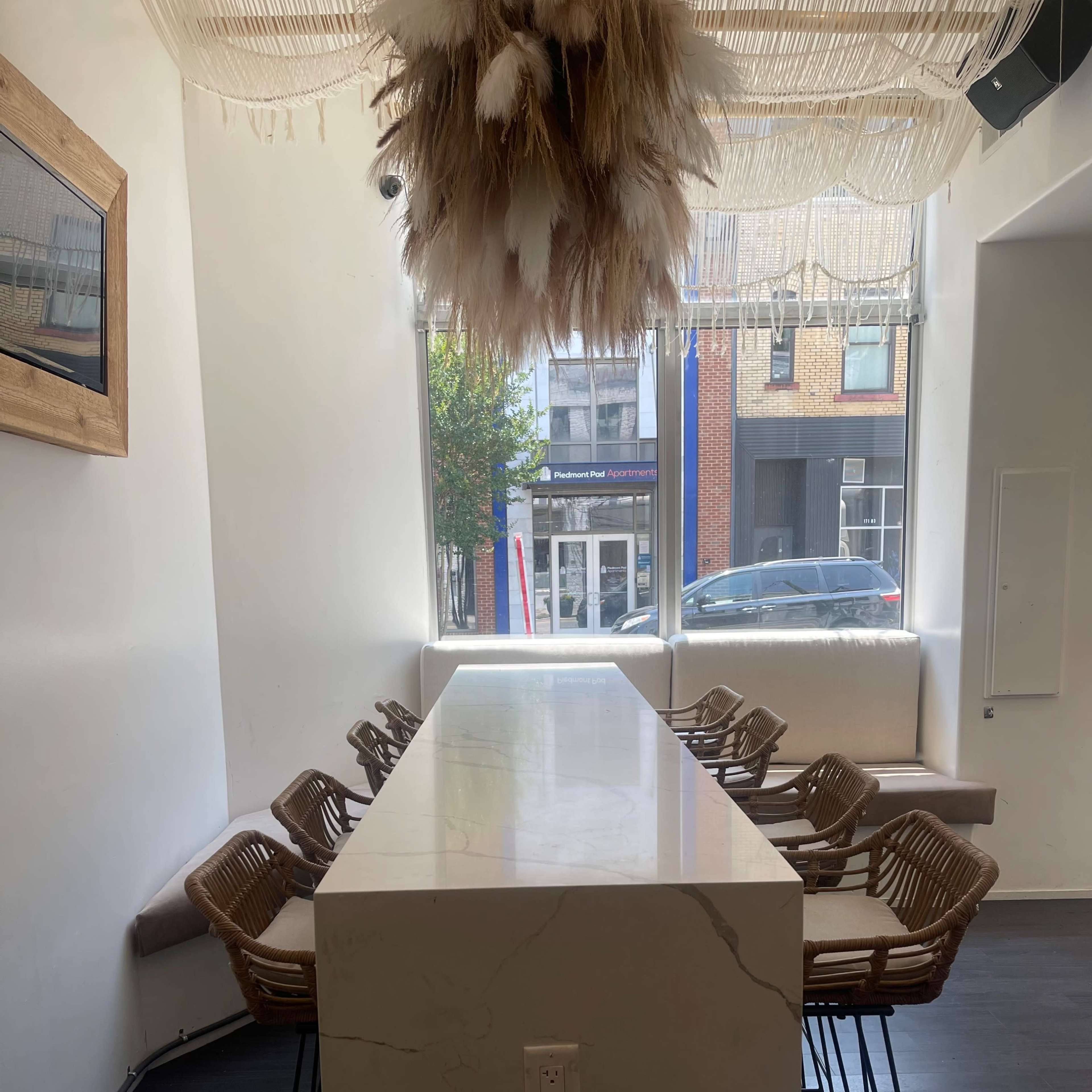 A modern dining area featuring a long marble table with rattan chairs and a decorative hanging arrangement.