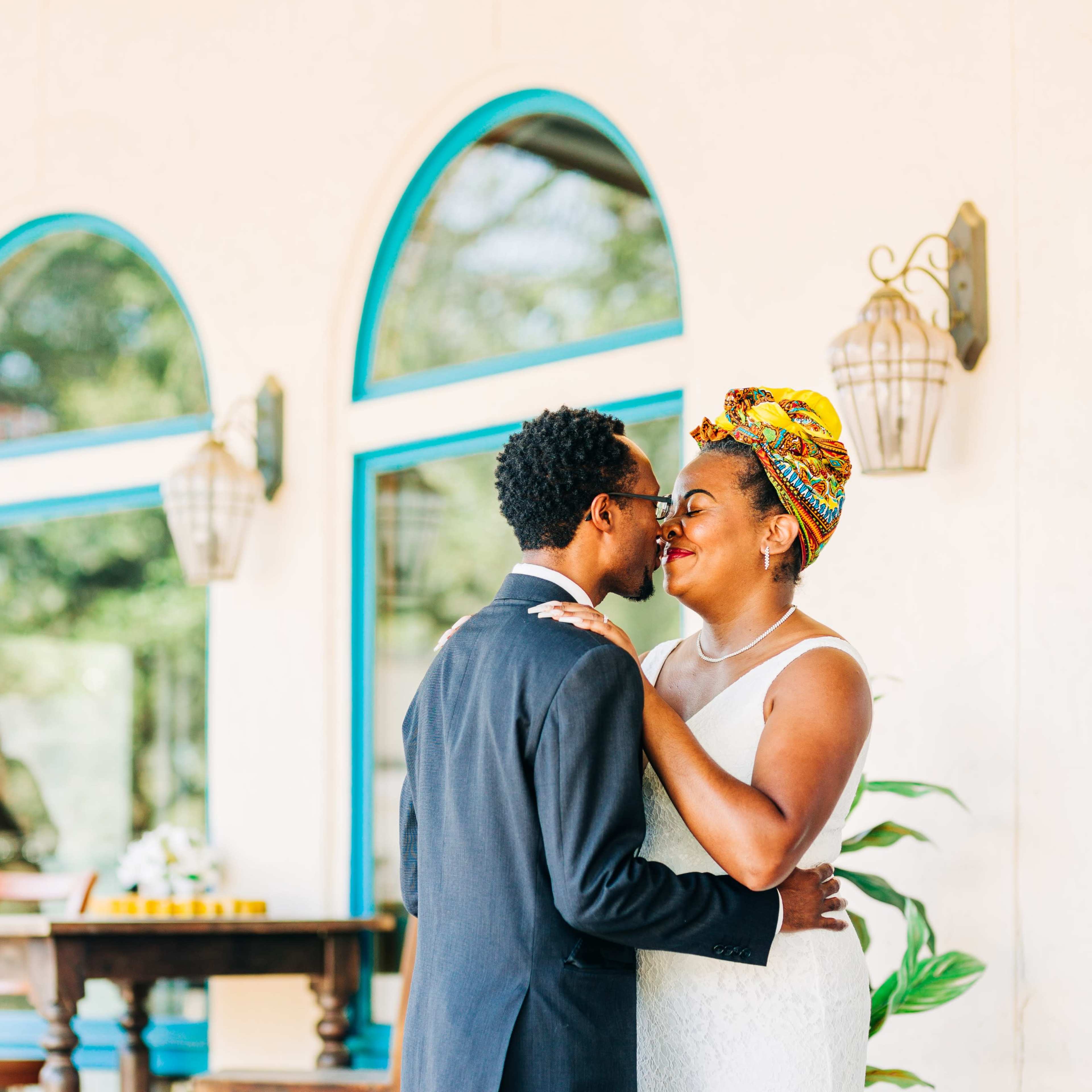 A couple stands close together under decorative lanterns outside a building with arched windows.