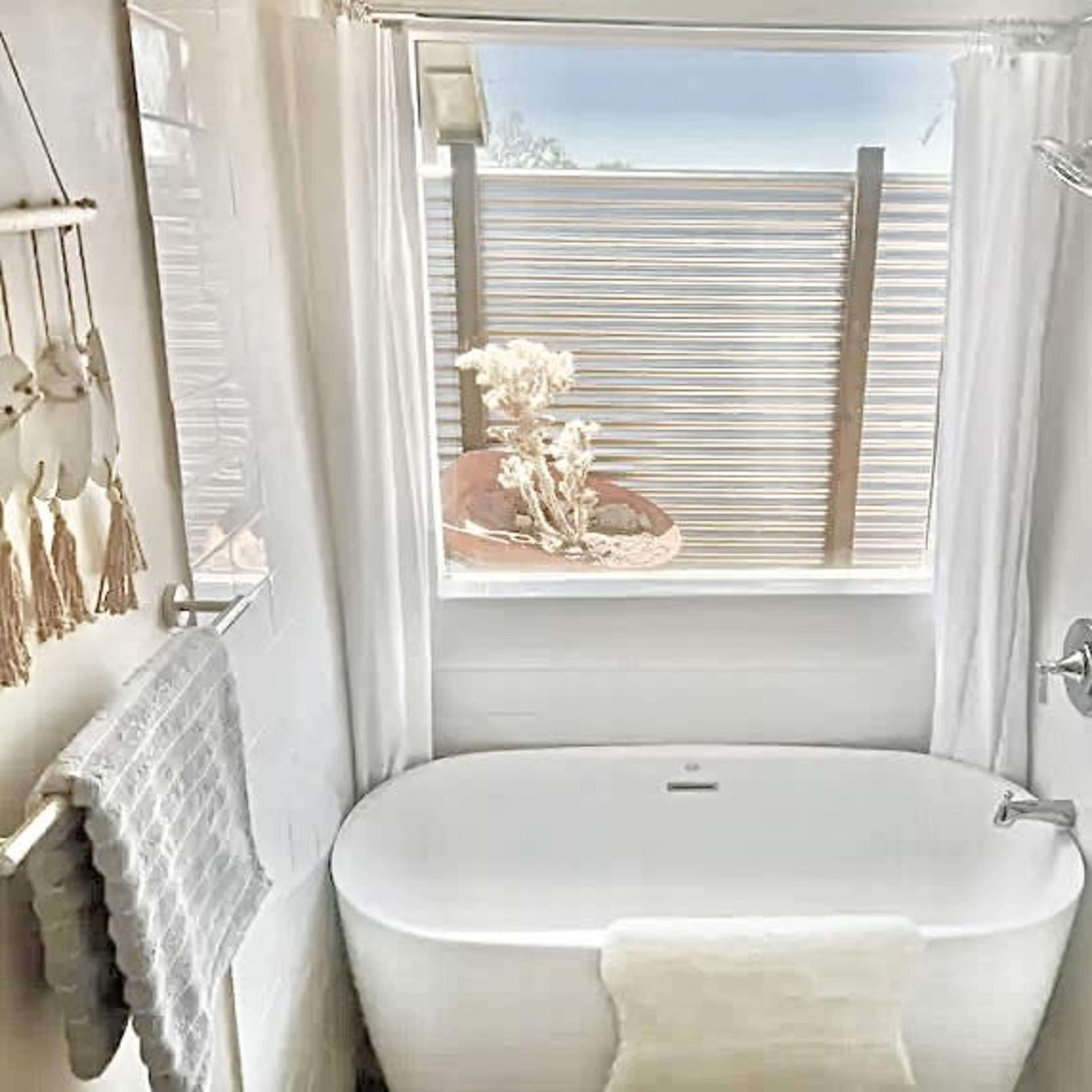 A bright bathroom features a freestanding tub with a view of a plant-filled outdoor area through the window.