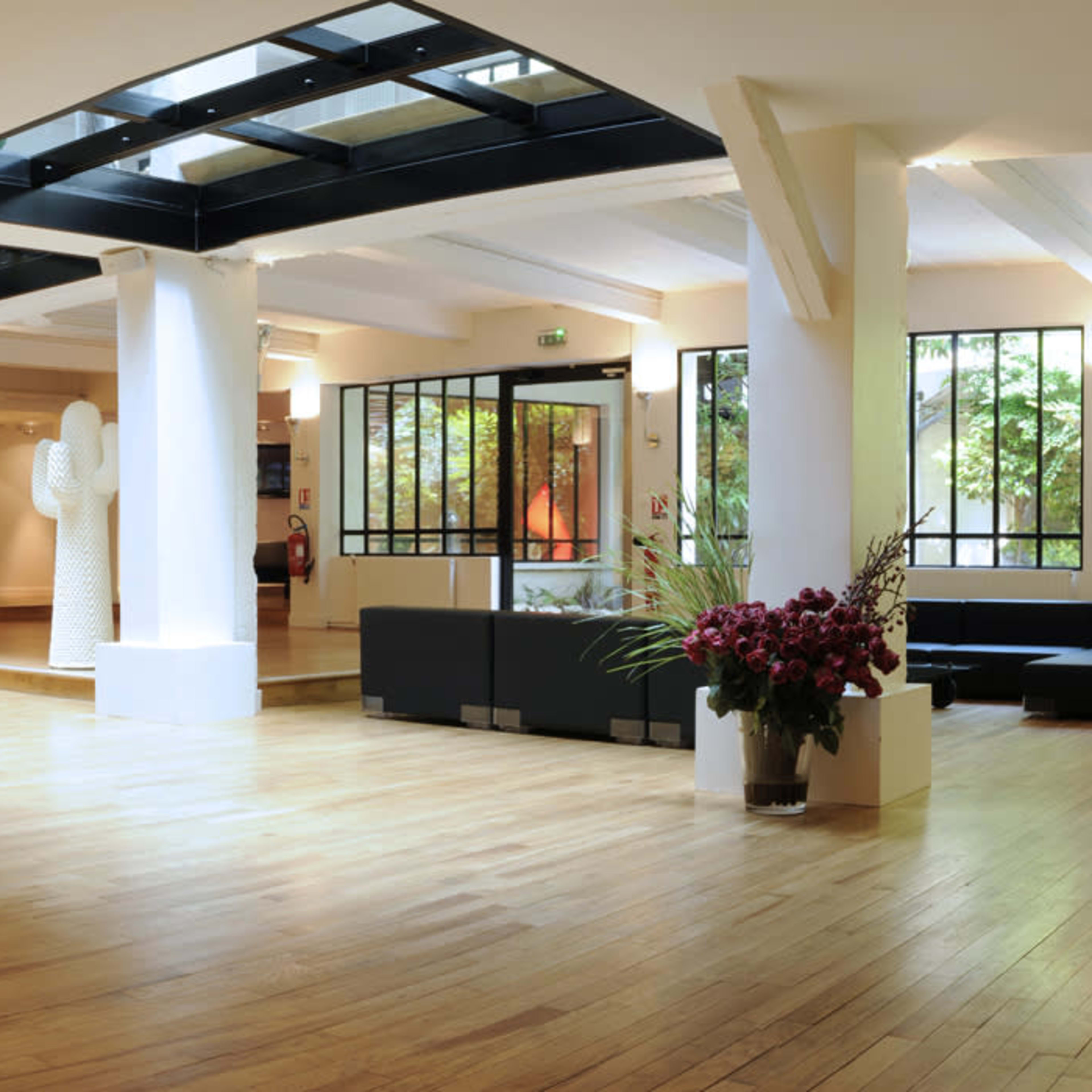A spacious interior room featuring wooden floors, large windows, and a spiral staircase, complemented by modern furniture and sculptures.