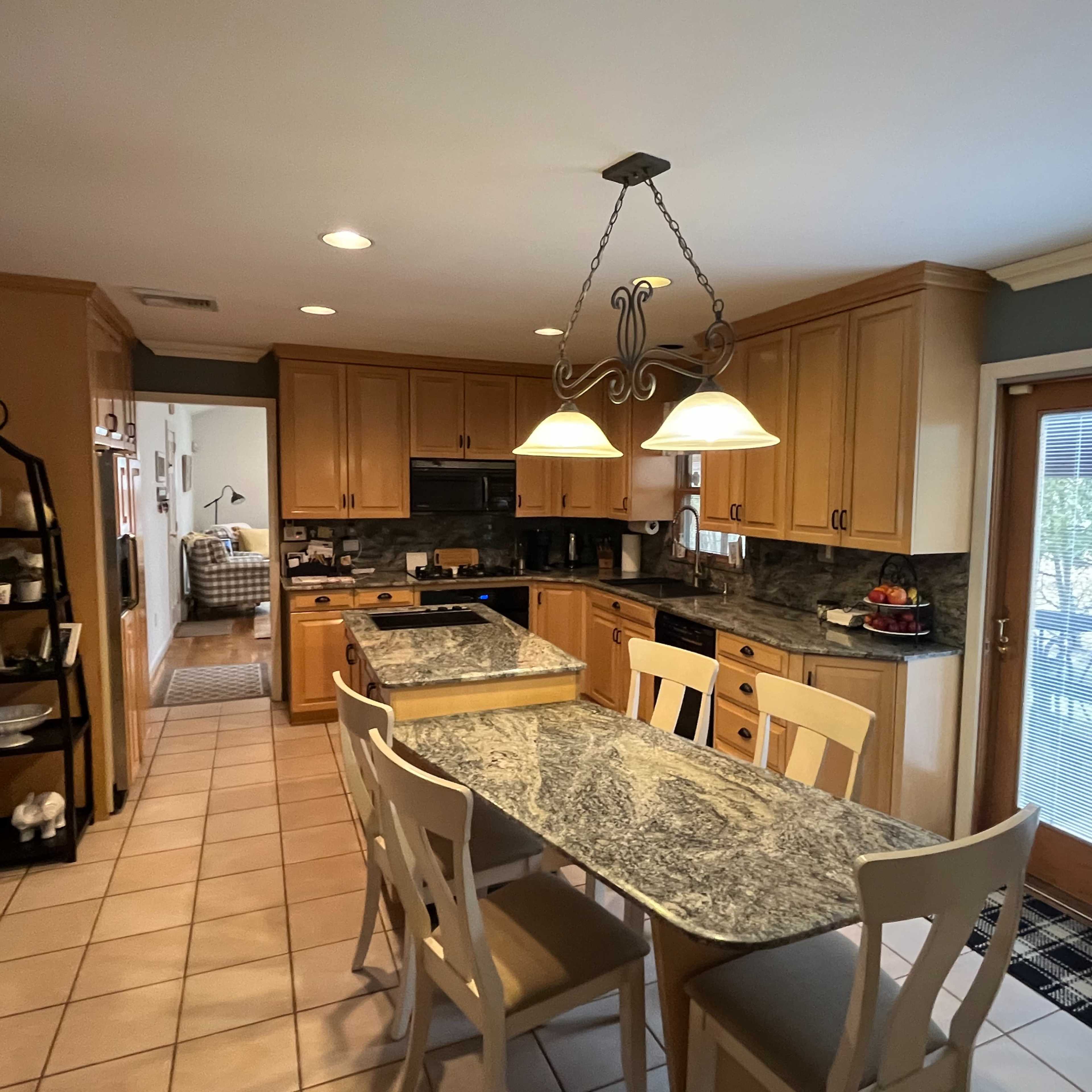 A spacious kitchen with wooden cabinets, a large granite dining table, and sliding glass doors leading to an outdoor area.