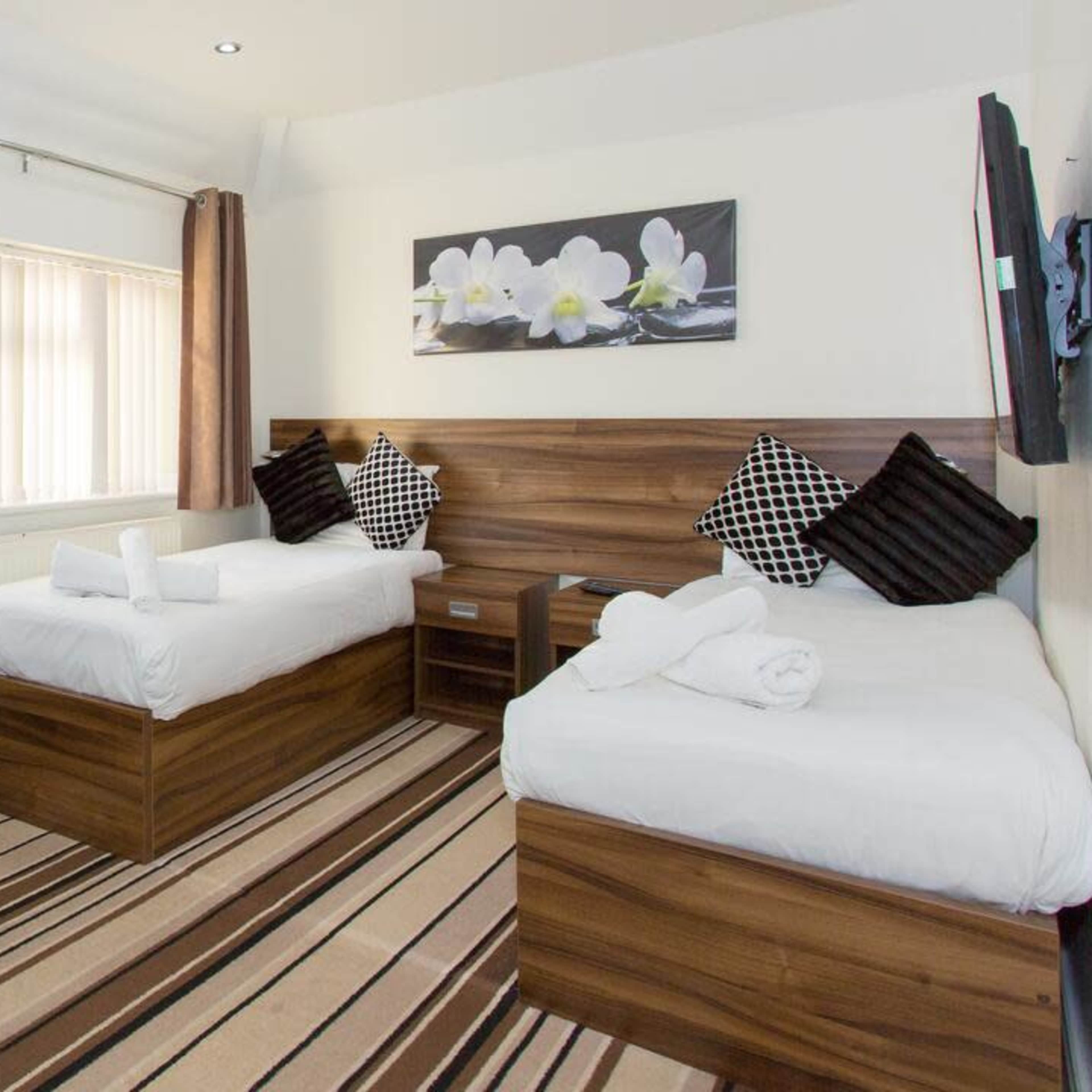 A well-furnished hotel room featuring two single beds, a desk with a chair, and a floral artwork on the wall.