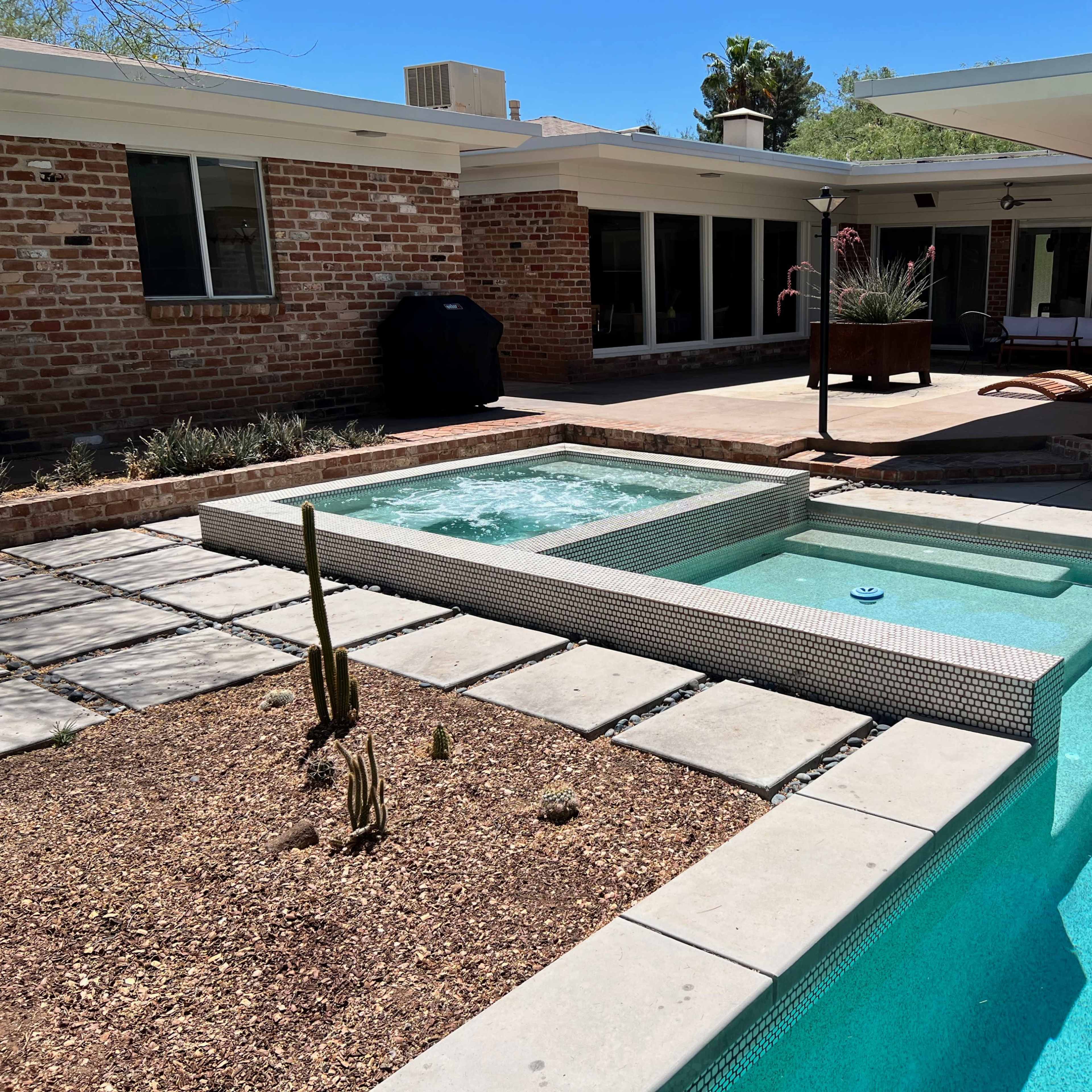 A backyard with a swimming pool and a spa, bordered by a patio and brick walls.