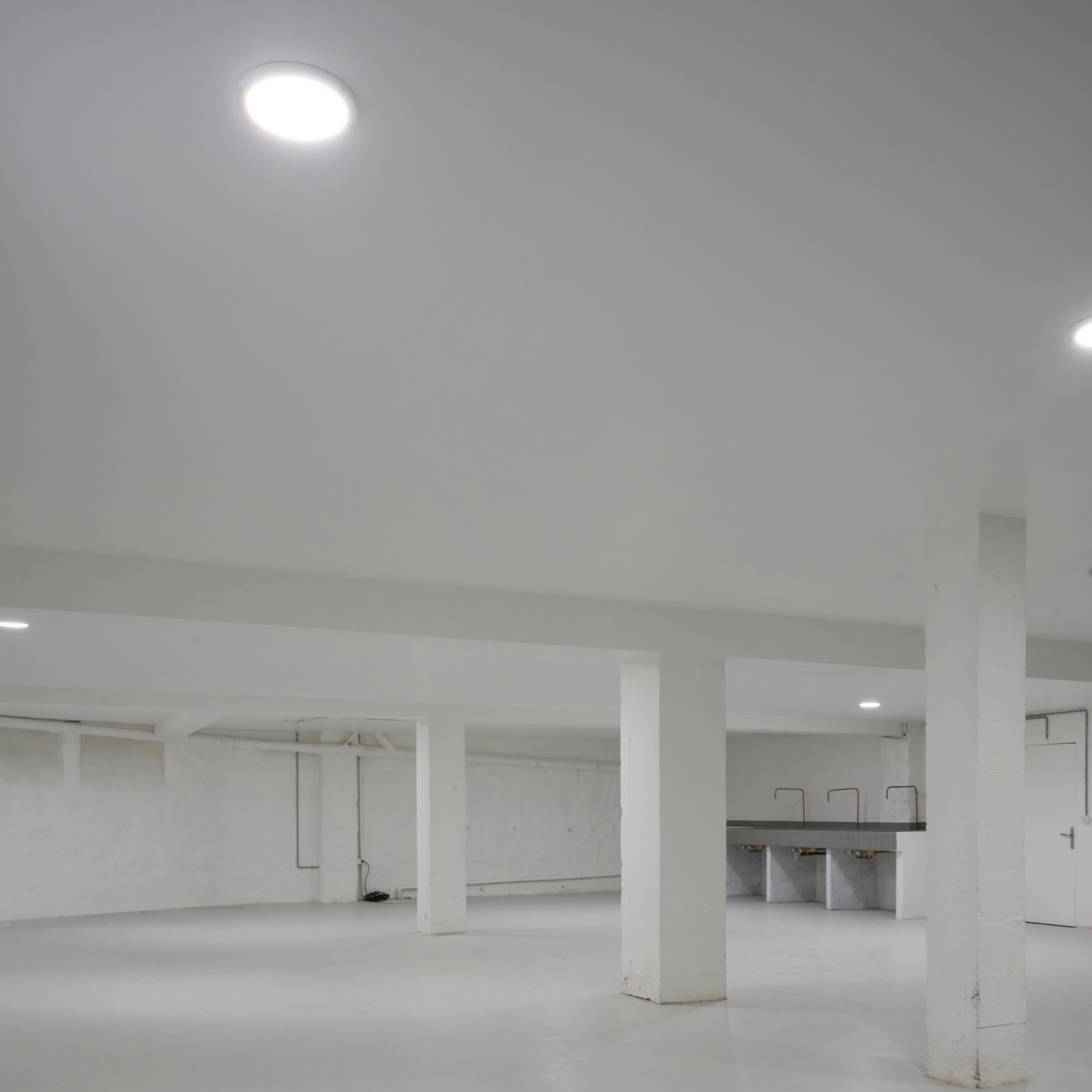A spacious, unfinished basement with white walls, concrete floors, and several supporting pillars.