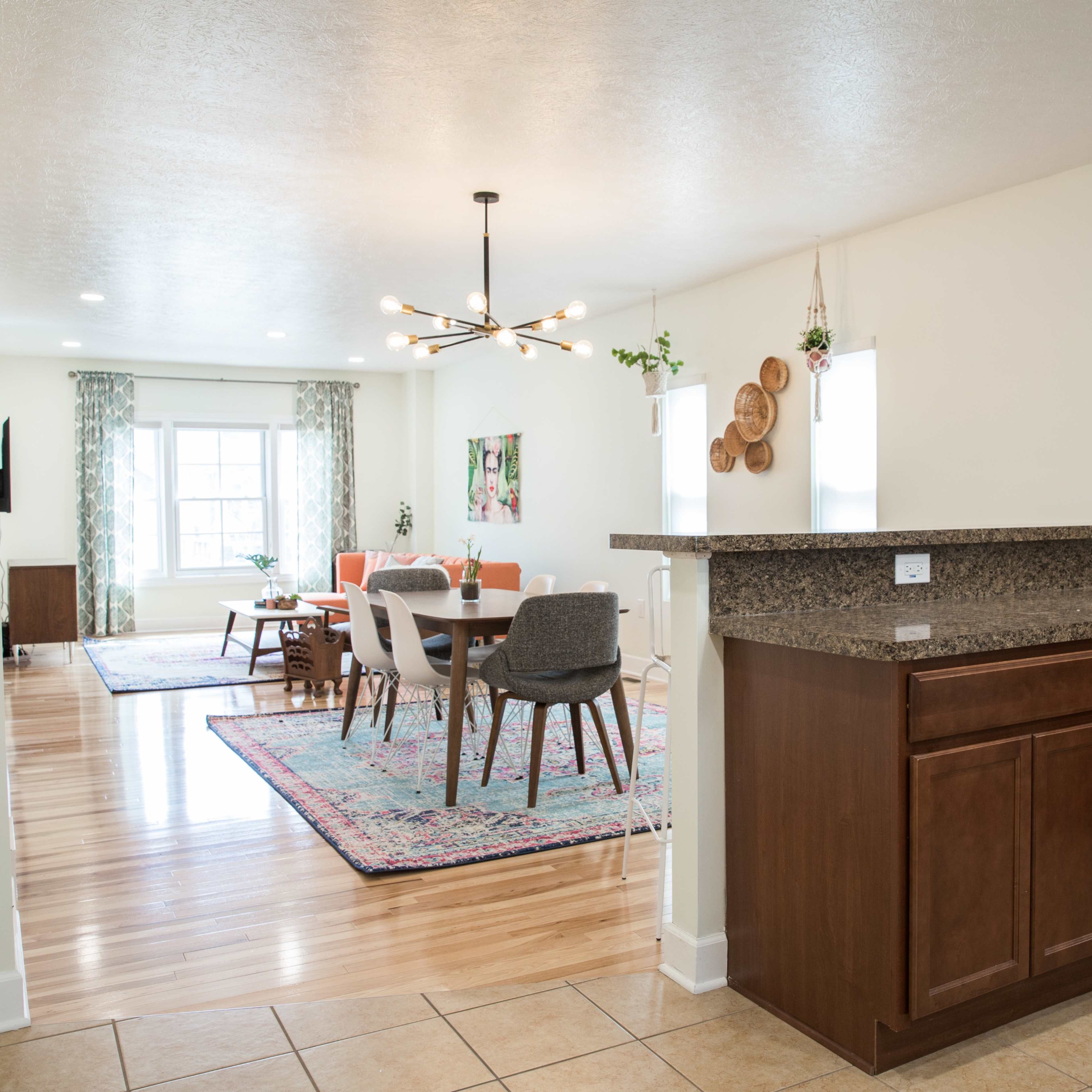 A kitchen area with a granite countertop open to a dining space featuring a table and chairs, illuminated by a modern light fixture.