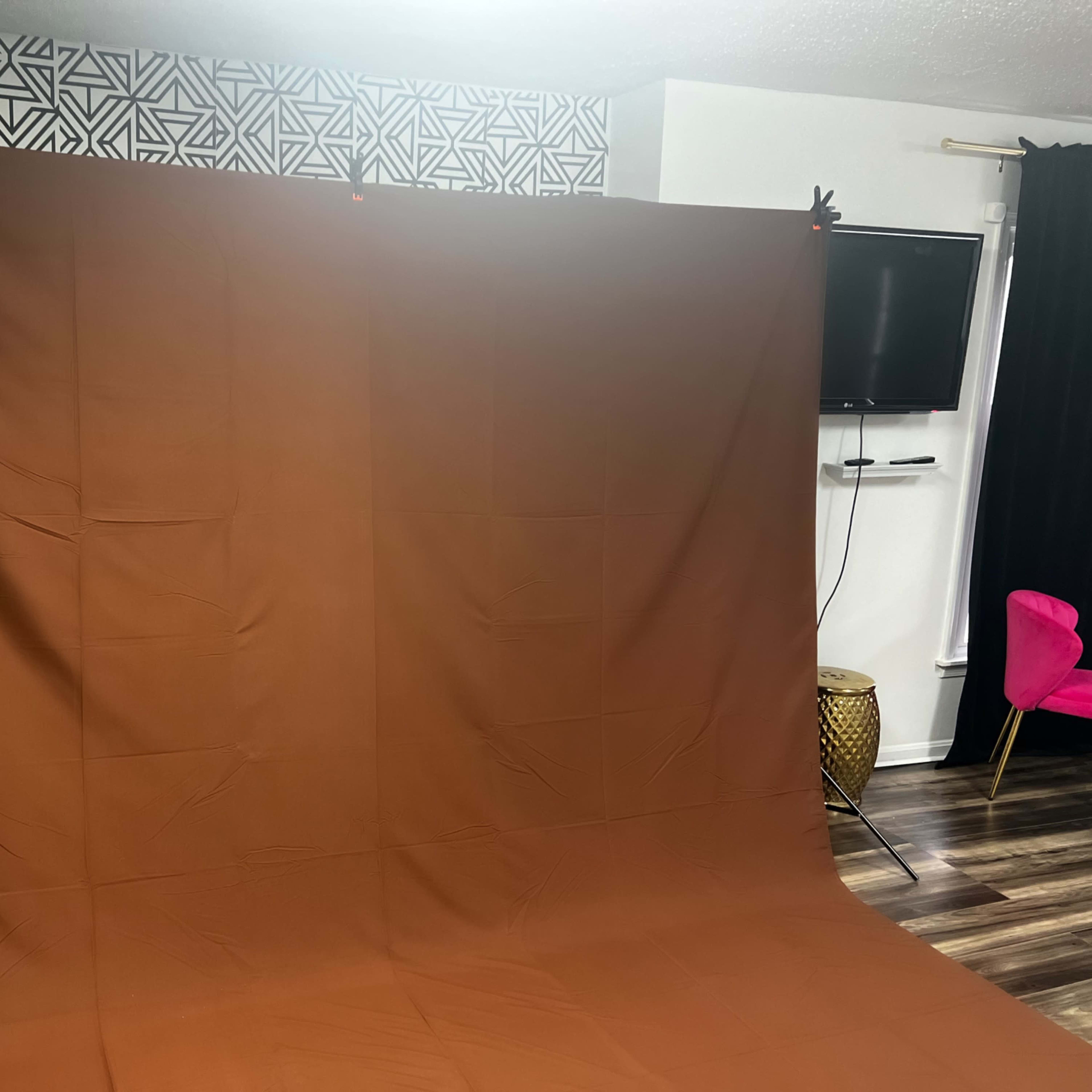 A studio setup featuring a large brown backdrop on a supporting frame, with a television and decorative elements in the background.