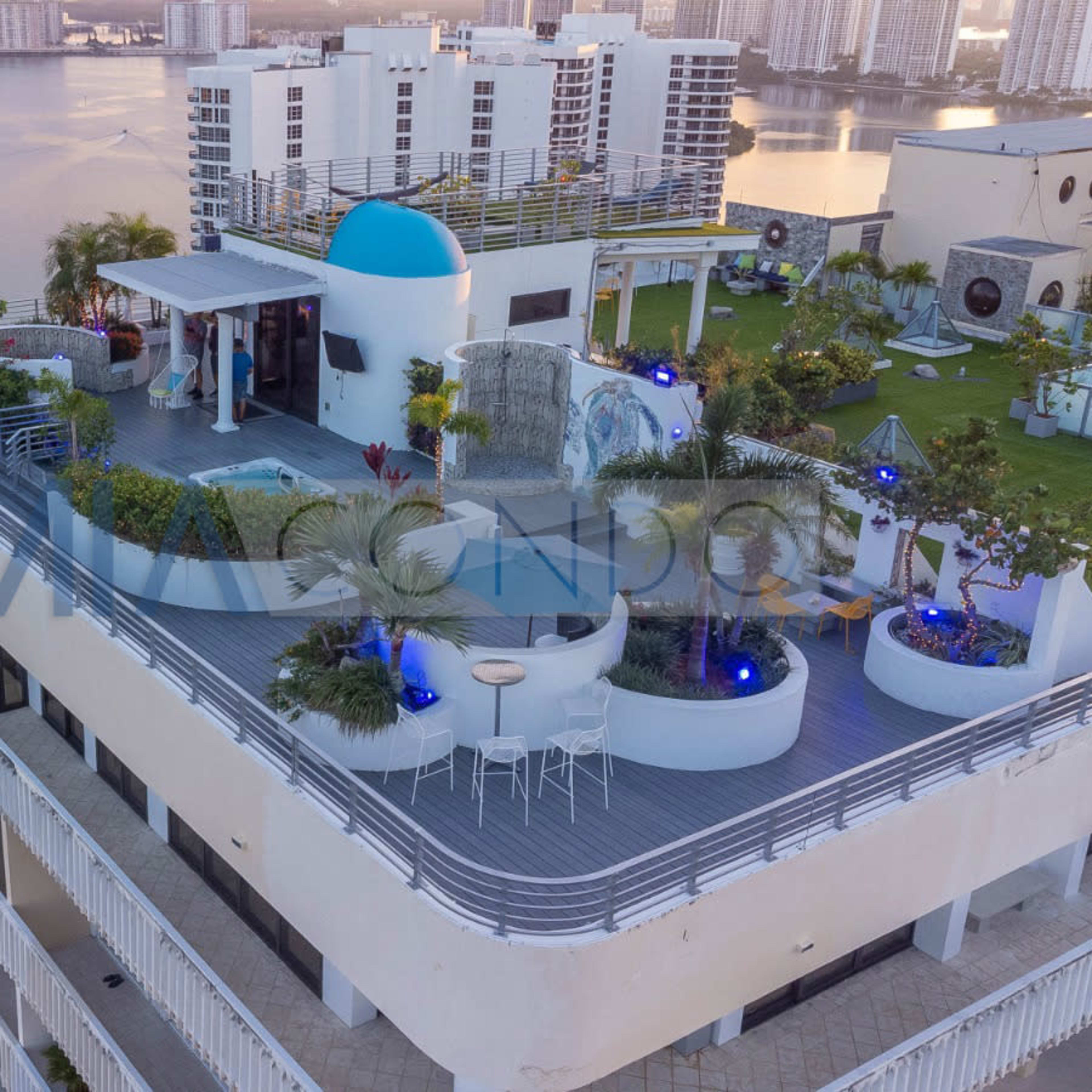 A rooftop terrace of a modern condominium featuring gardens, seating areas, and a blue dome against a backdrop of a waterfront city skyline.