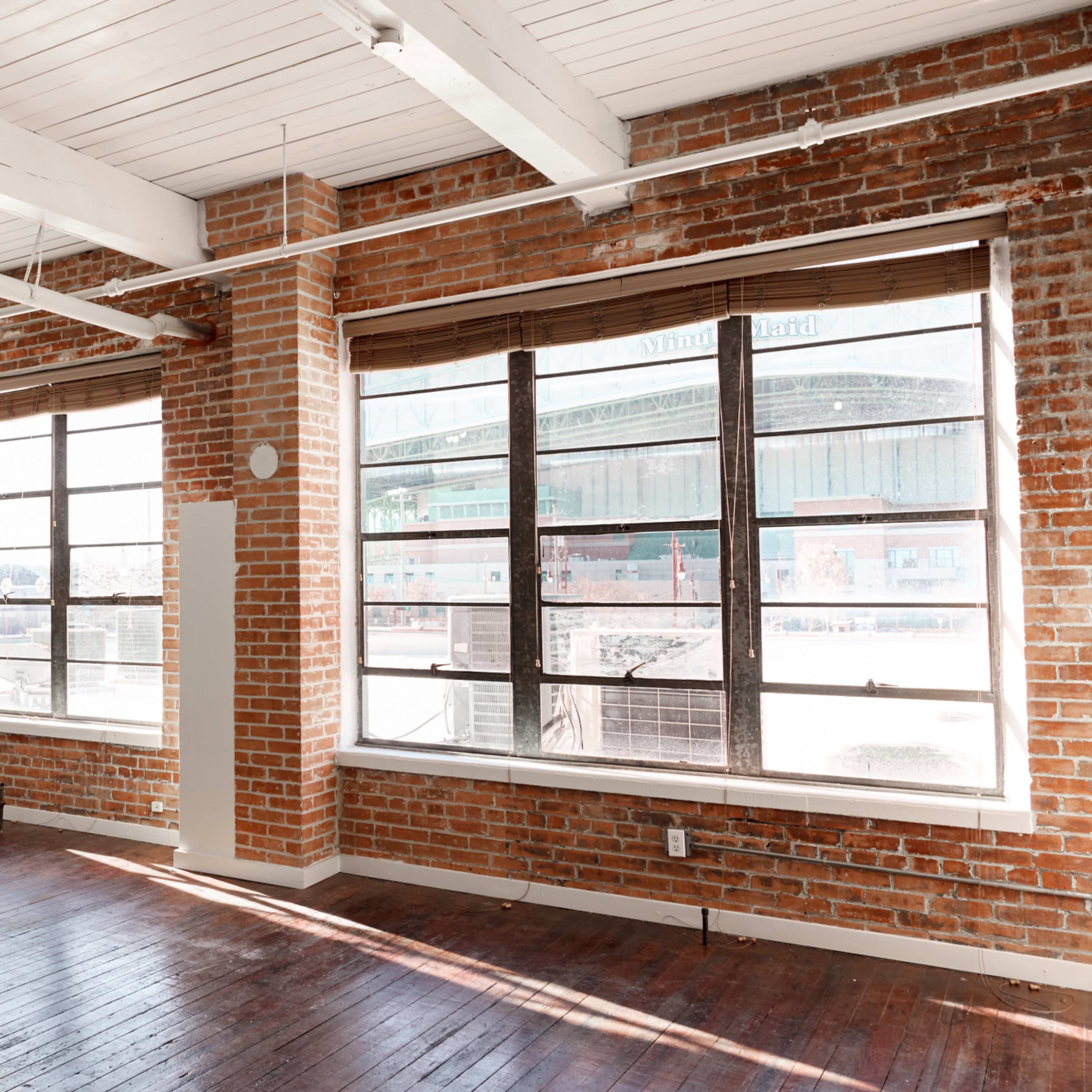 A spacious interior with exposed brick walls, large windows, and wooden flooring.