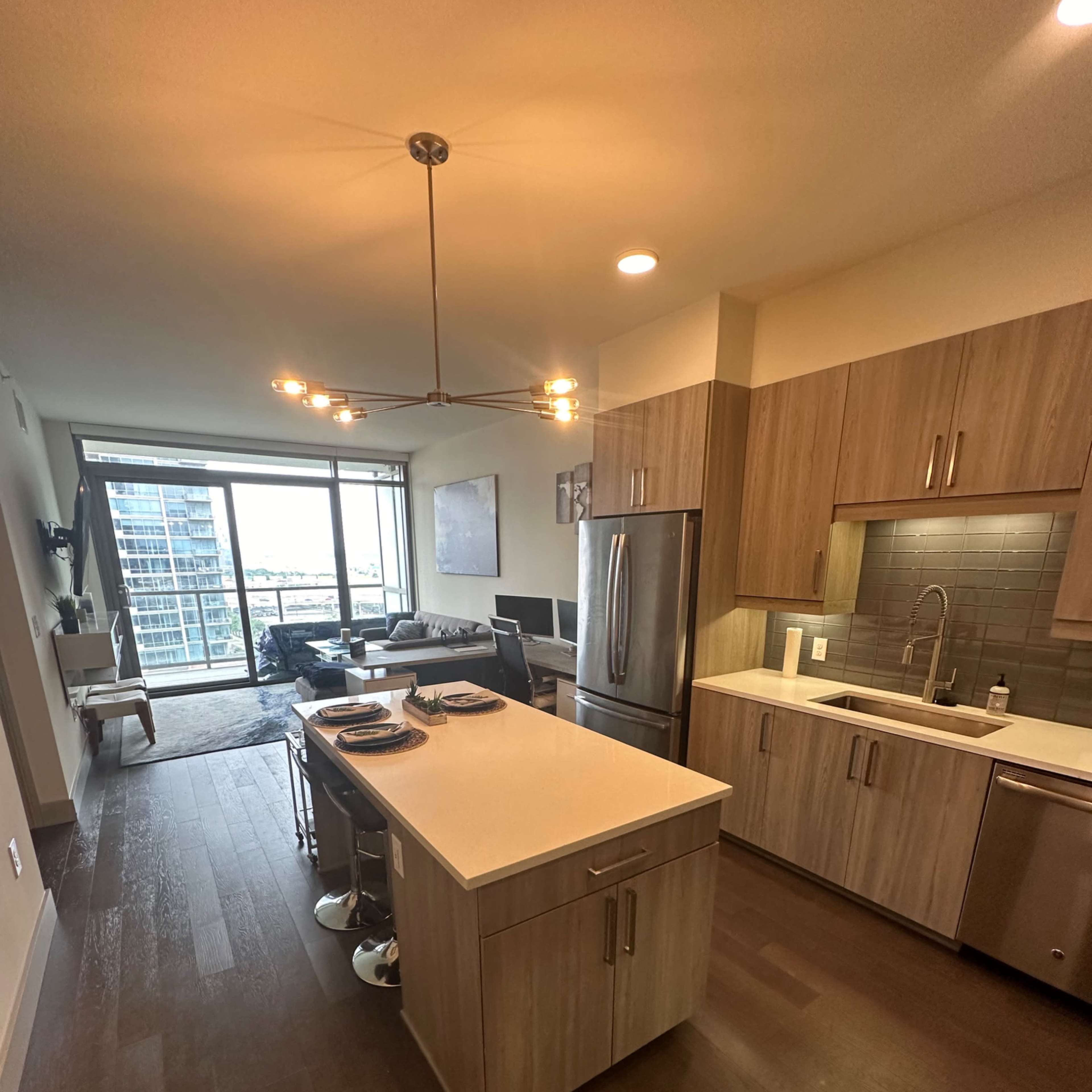 A modern kitchen with an island, stainless steel appliances, and large windows overlooking a city view.