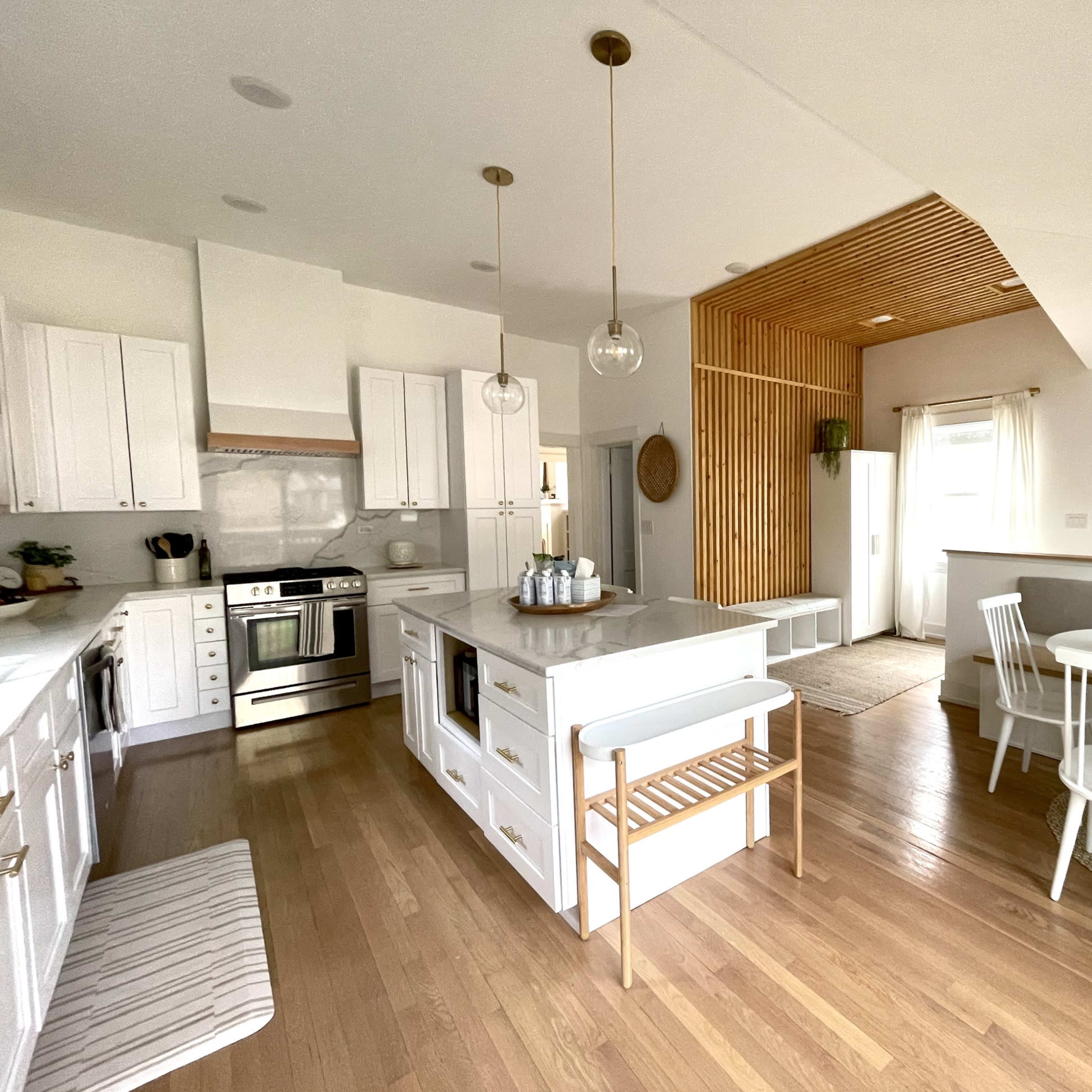 A modern kitchen with white cabinetry, a central island, and a dining area featuring a round table and white chairs.